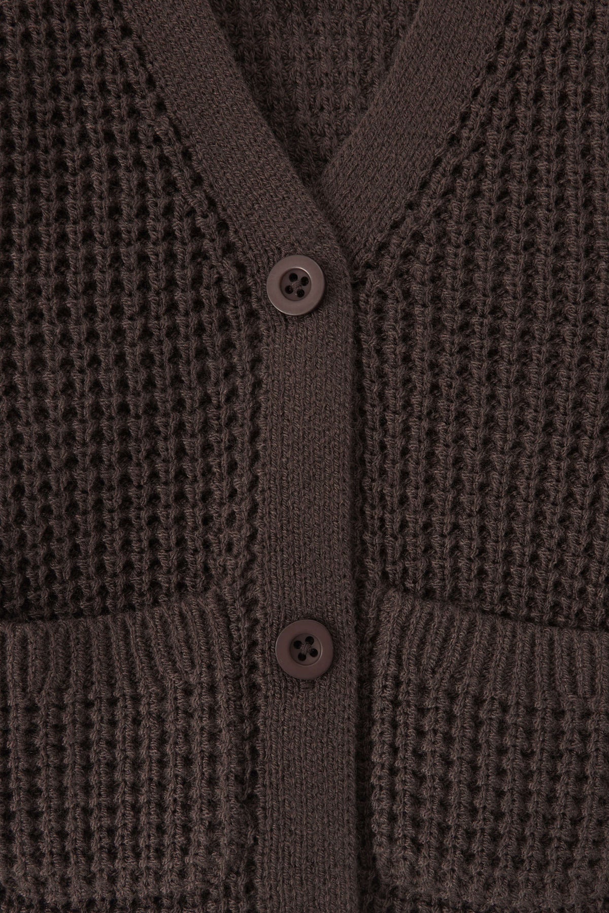 Close-up of a textured knit cardigan in a dark brown color, featuring a waffle-weave pattern, ribbed trim, and two white buttons.