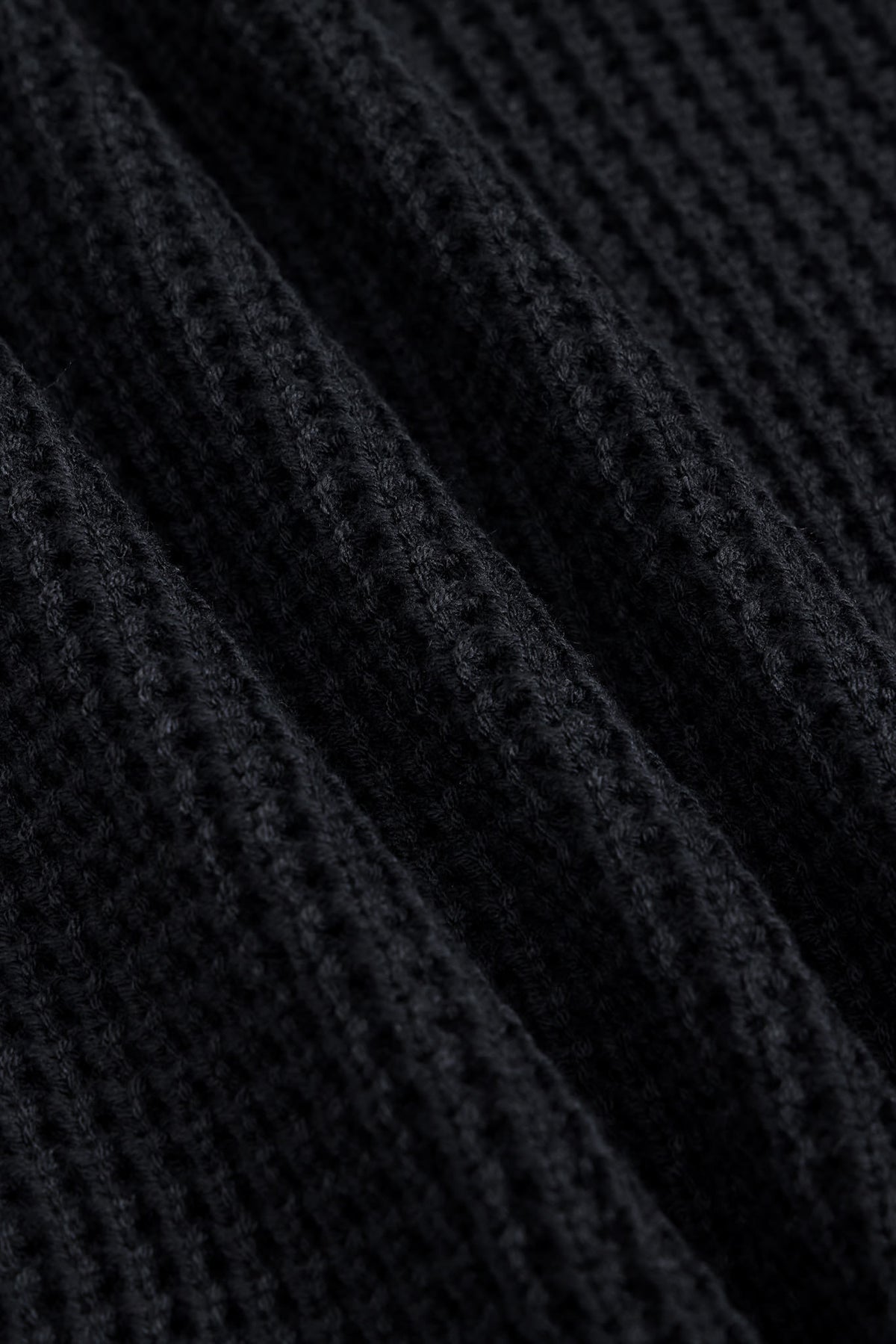 Close-up of a black ribbed knit fabric with a waffle or textured weave, shown in soft diagonal folds.