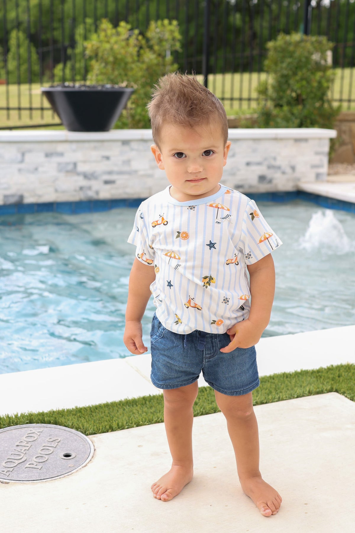 Young boy standing by the pool edge wearing the Toddler Basic Tee in Amalfi Coast with jean shorts