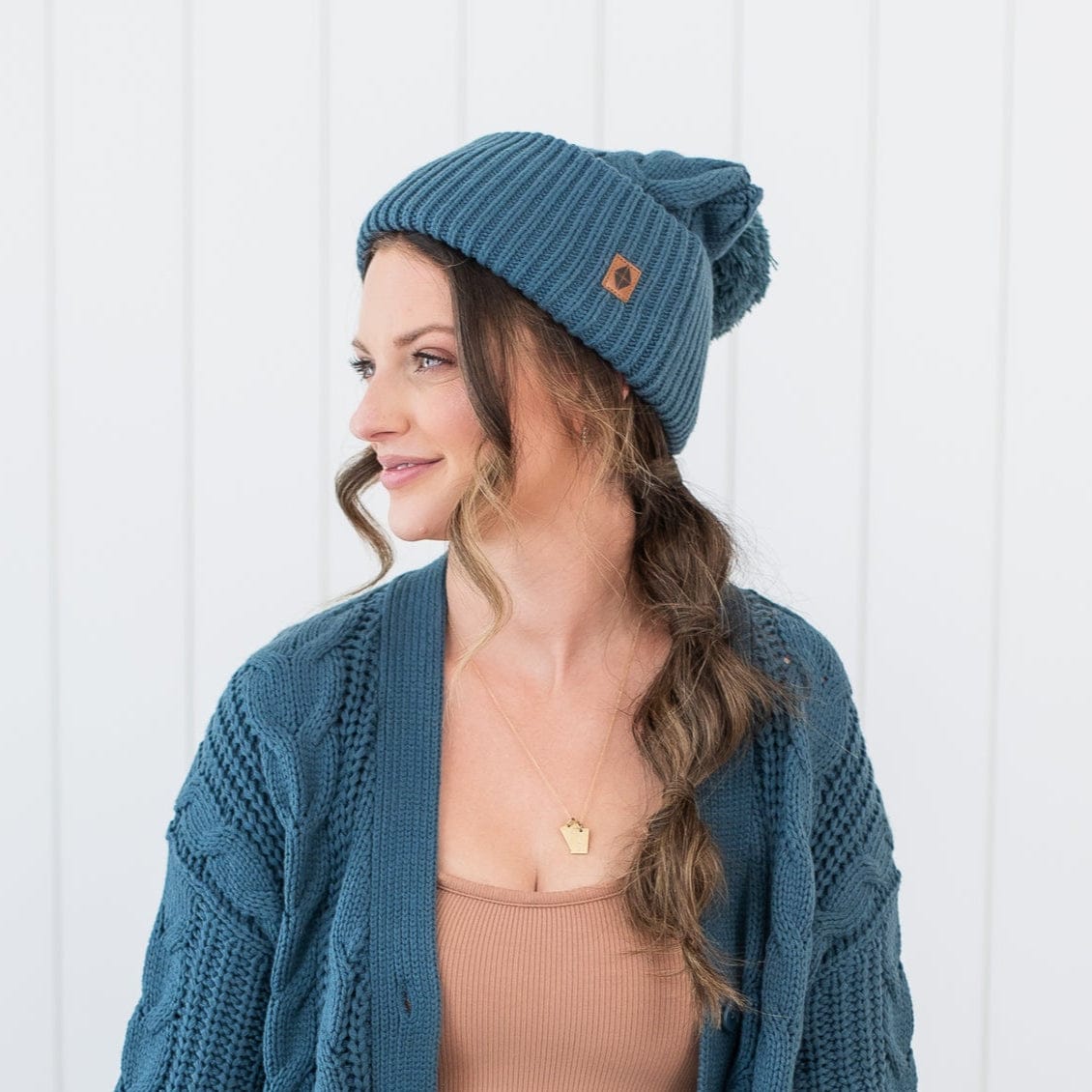 Female model wearing the Cable Knit Adult Cardigan in Atlantic with matching cable knit pom beanie with a Latte Cami Dress on