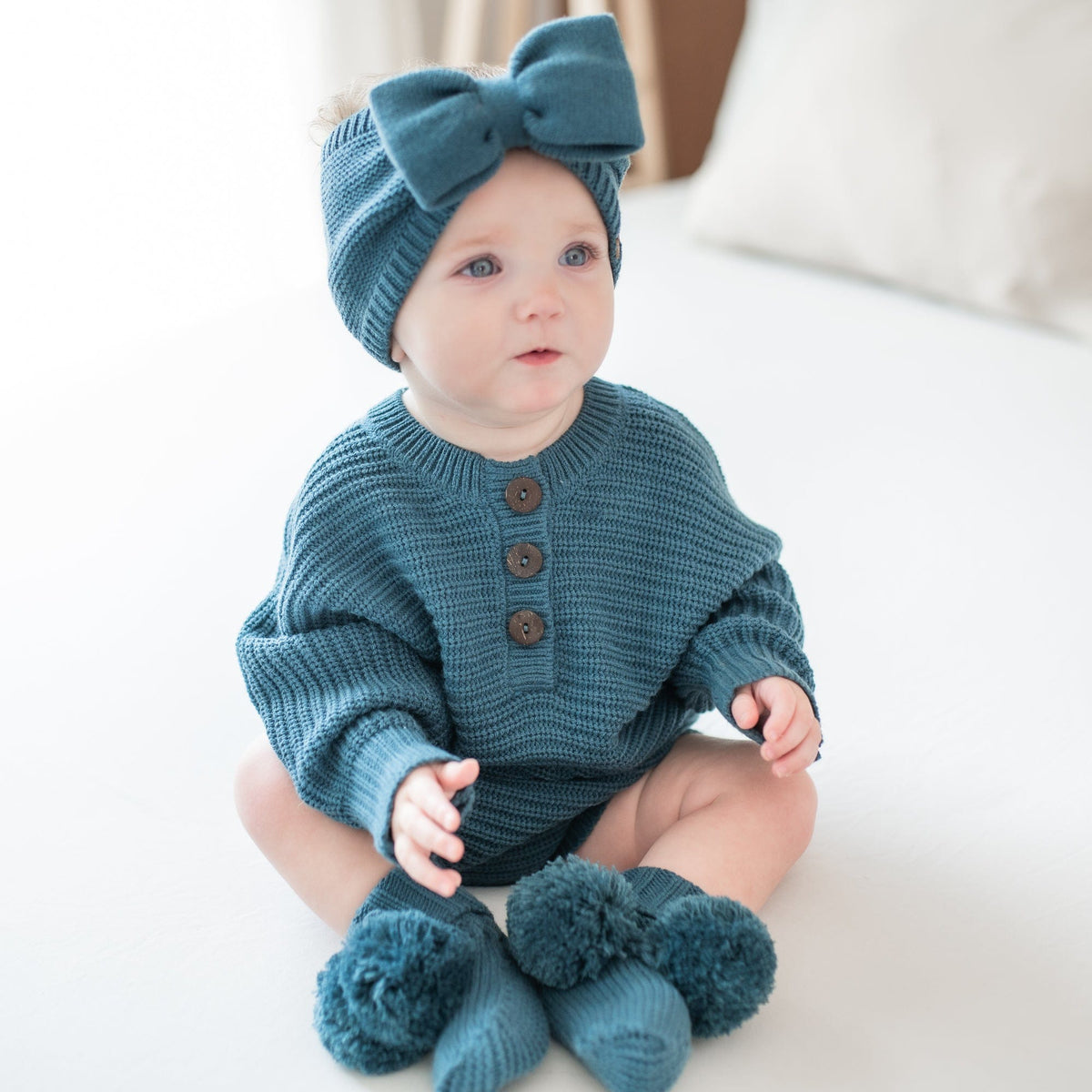 Infant sitting wearing the Chunky Knit Bow Headband in Atlantic and matching chunky knit romper and knit booties