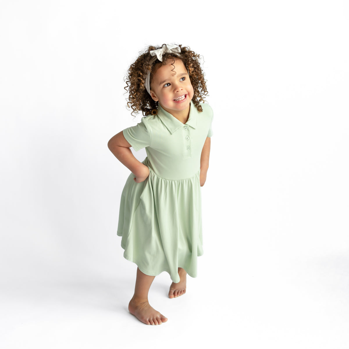Smiling girl posing wearing the Polo Dress in Basil in front of a white background