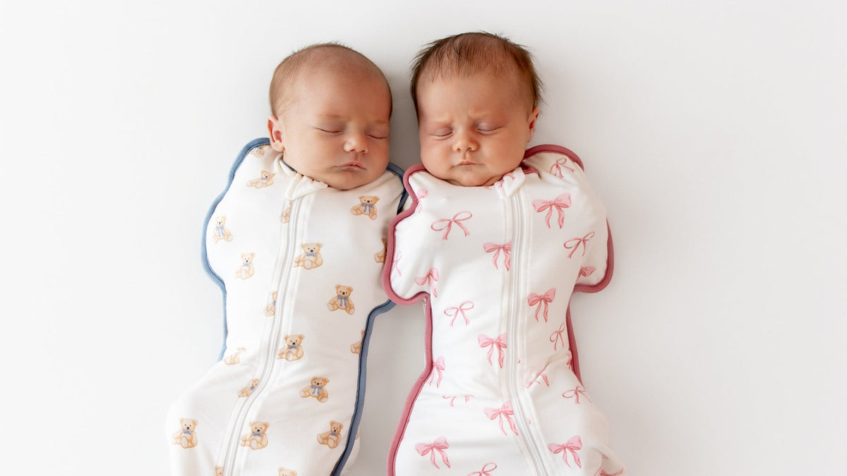 Two sleeping babies wearing swaddle bags in teddy bear and bow print