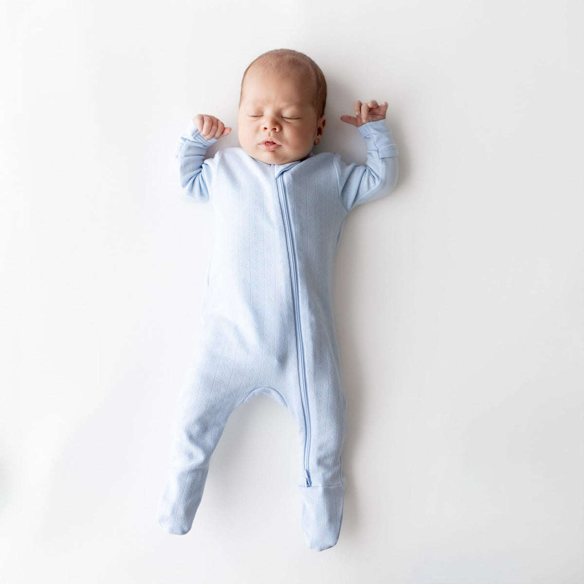 Sleeping newborn wearing the Pointelle Zippered Footie in Breeze