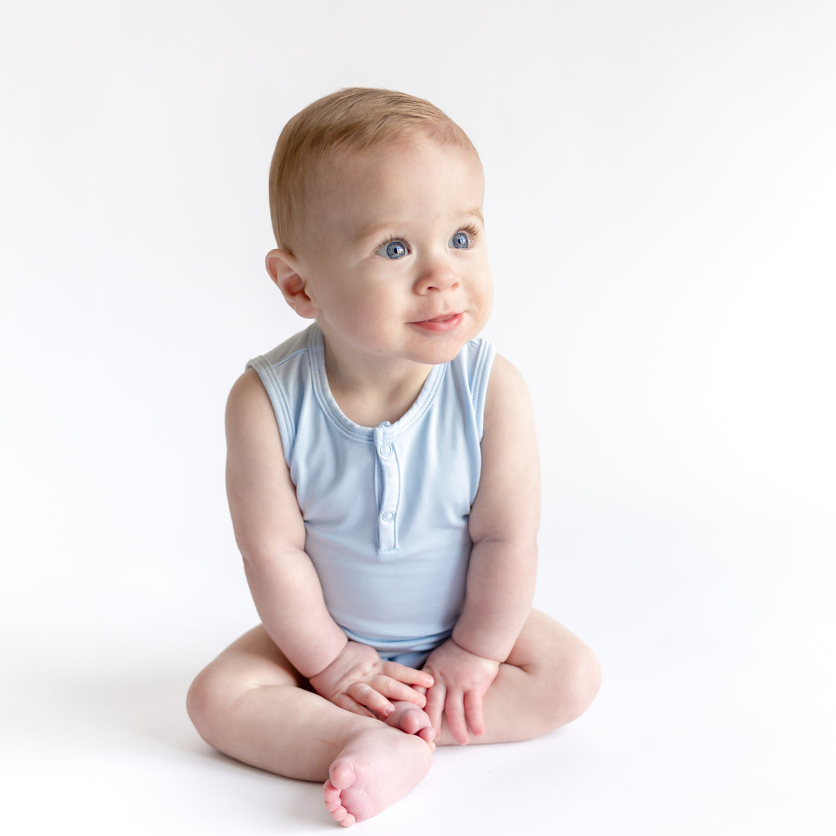 Young toddler sitting on the floor wearing the Sleeveless Bodysuit in Breeze
