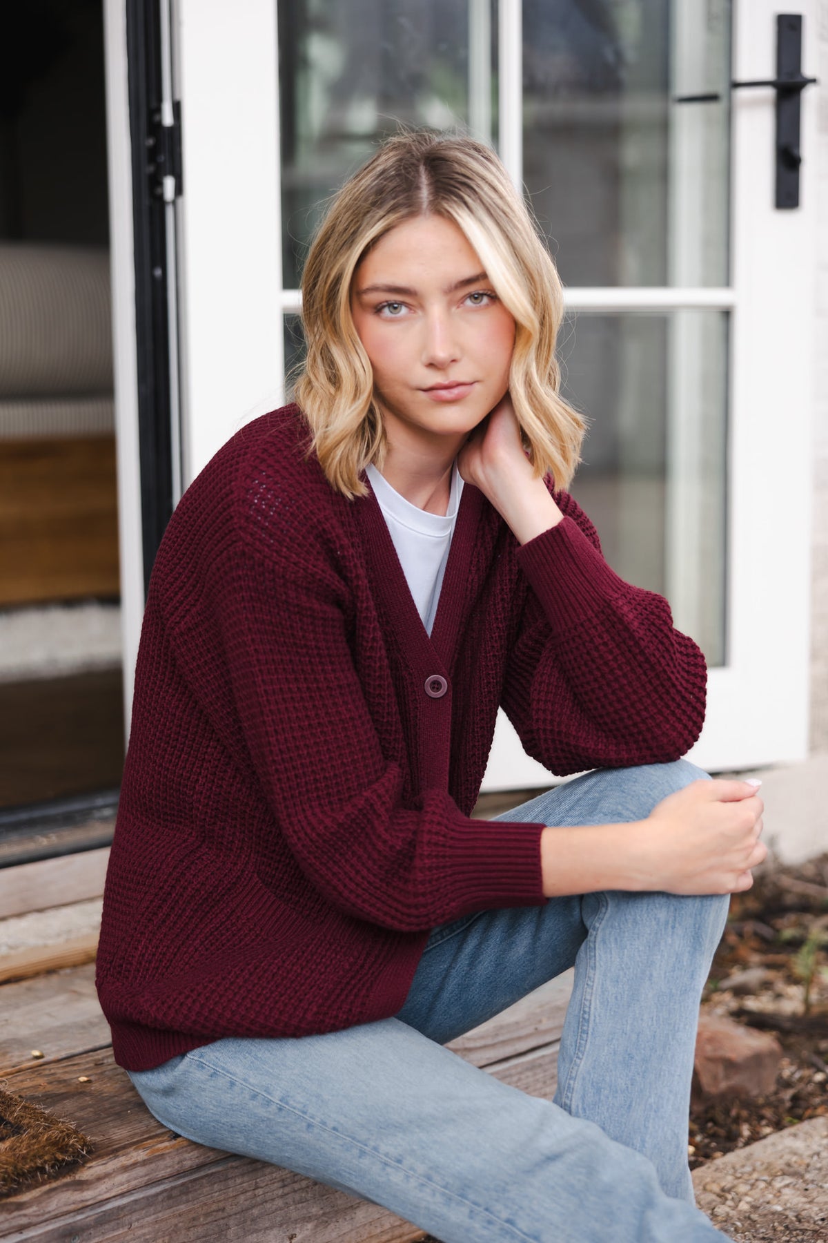 Modal posing outdoors wearing Chunky Knit Women's Waffle Cardigan in Burgundy over white T-shirt and blue jeans