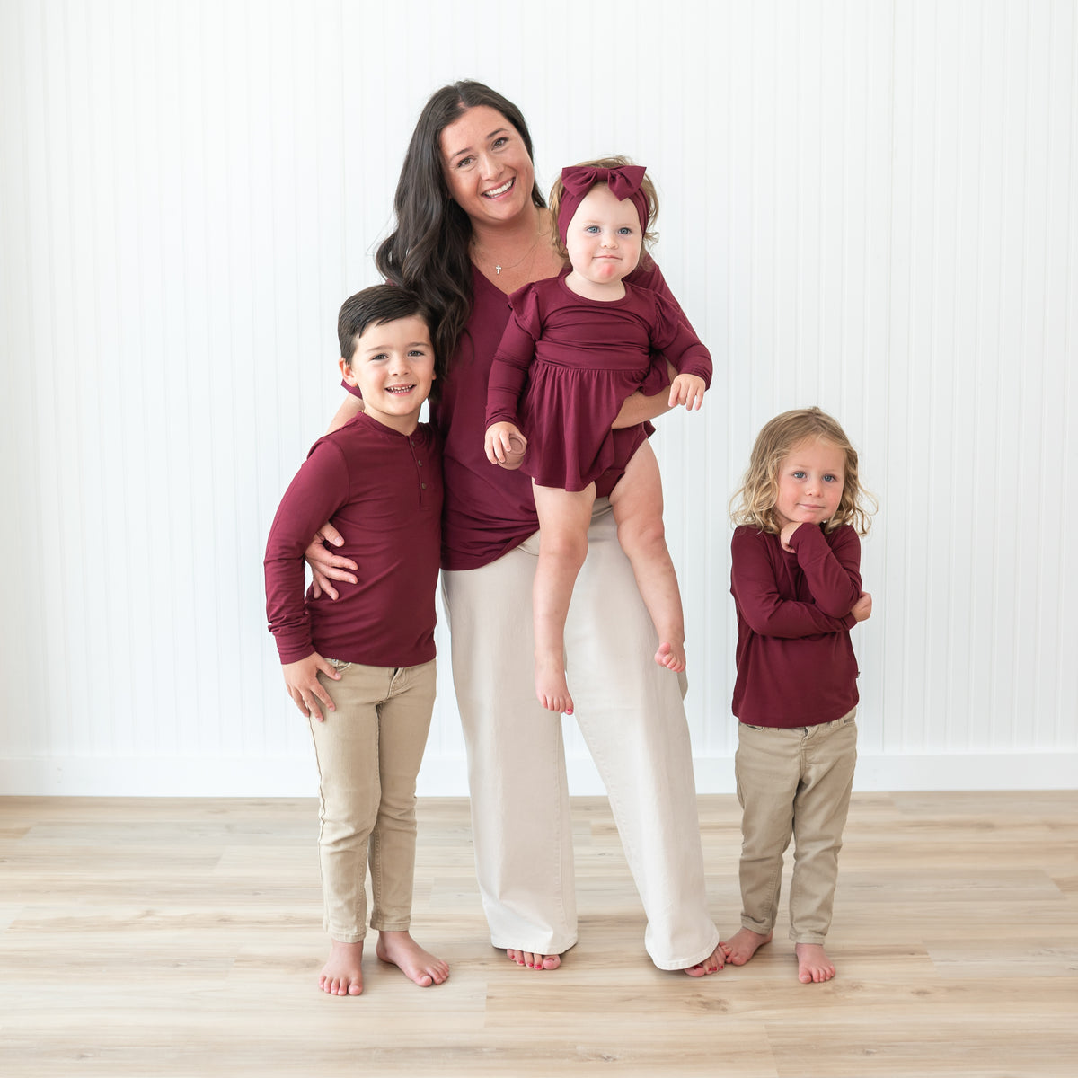 Family matching in Burgundy. Pictured is the women's v-neck, Long Sleeve Twirl Bodysuit Dress, long sleeve toddler crew neck and the toddler long sleeve henley top
