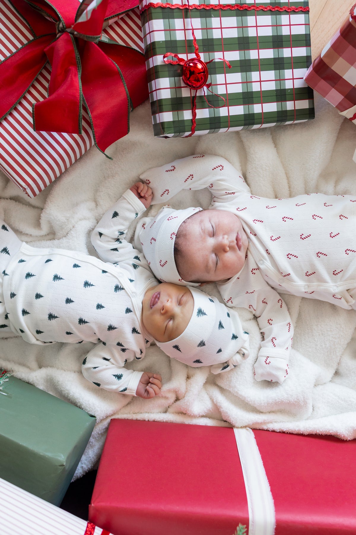 Two babies wearing Pointelle Take Me Home Set with Cap in Candy Cane and Christmas Tree sleeping between presents