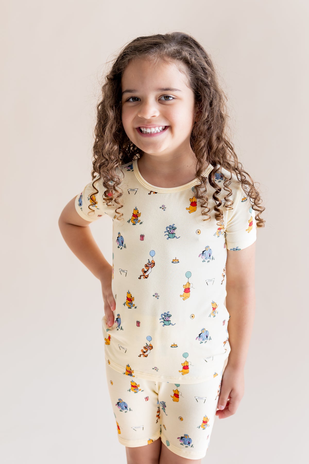 Girl smiling in Short Sleeve Pajamas in Winnie the Pooh Celebration print on a cream background