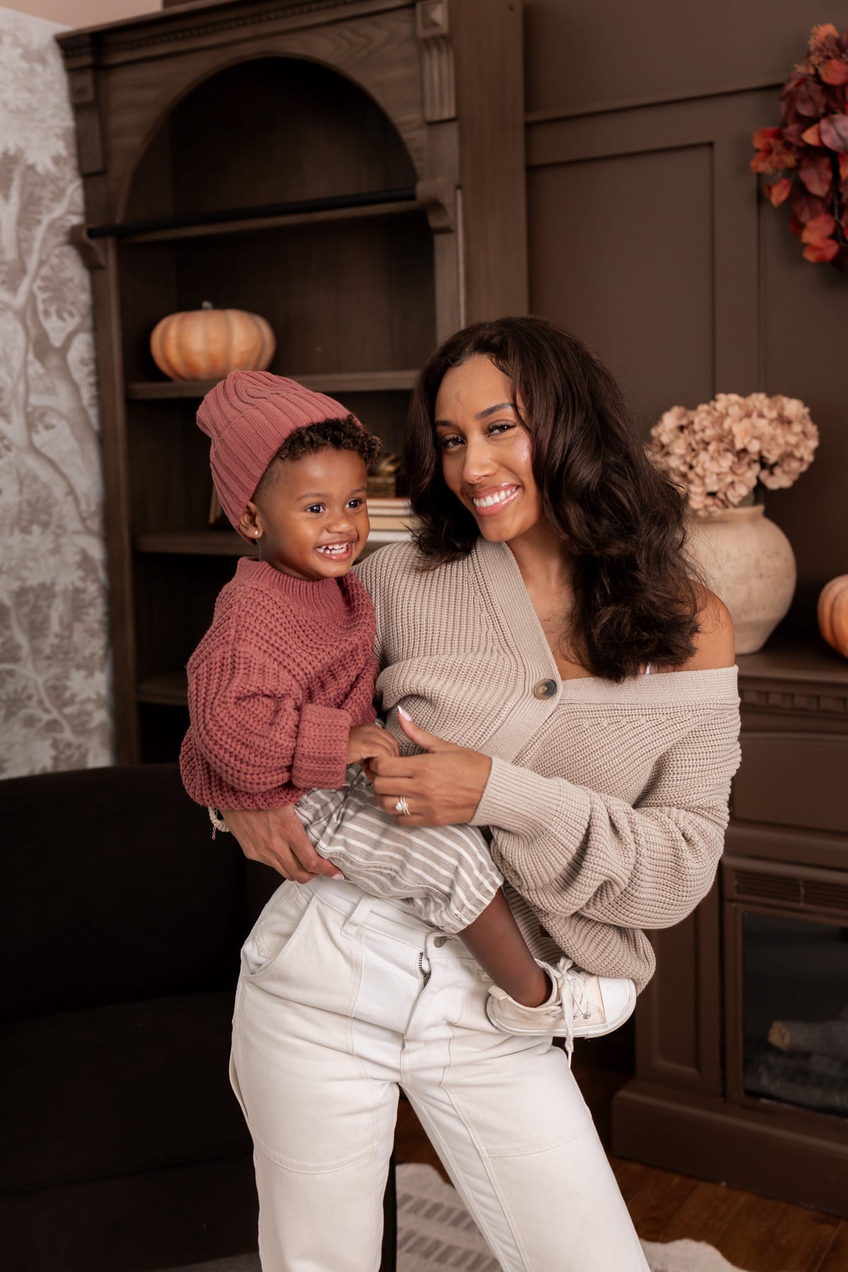 Modal wearing Chunky Knit Women's Cropped Cardigan in Almond with child wearing chunky knit ribbed beanie and Chunky knit sweater in espresso sitting in al living room