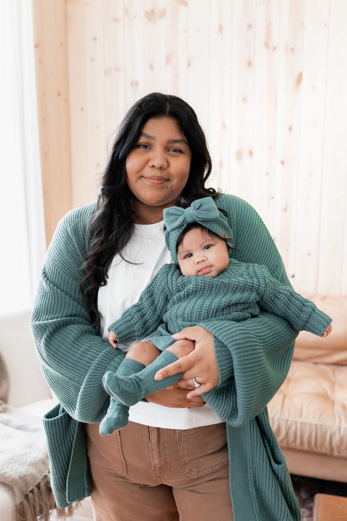 Modal wearing Chunky Knit Women's Oversized Cardigan in Pine with baby wearing Chunky knit sweater, chunky knit bow headband and socks in pine