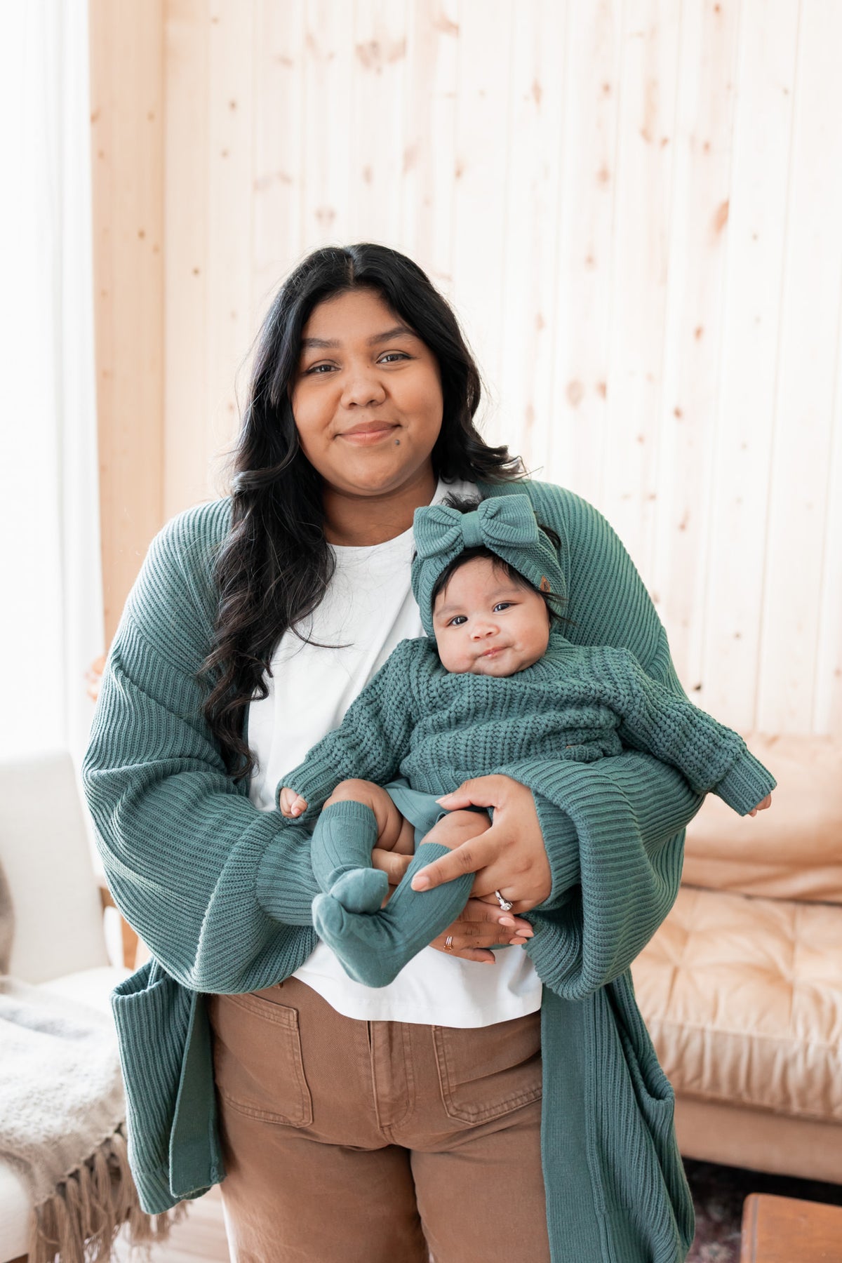 Modal wearing Chunky Knit Women's Oversized Cardigan In Pine with baby wearing Chunky knit sweater, chunky knit bow headband and socks in pine