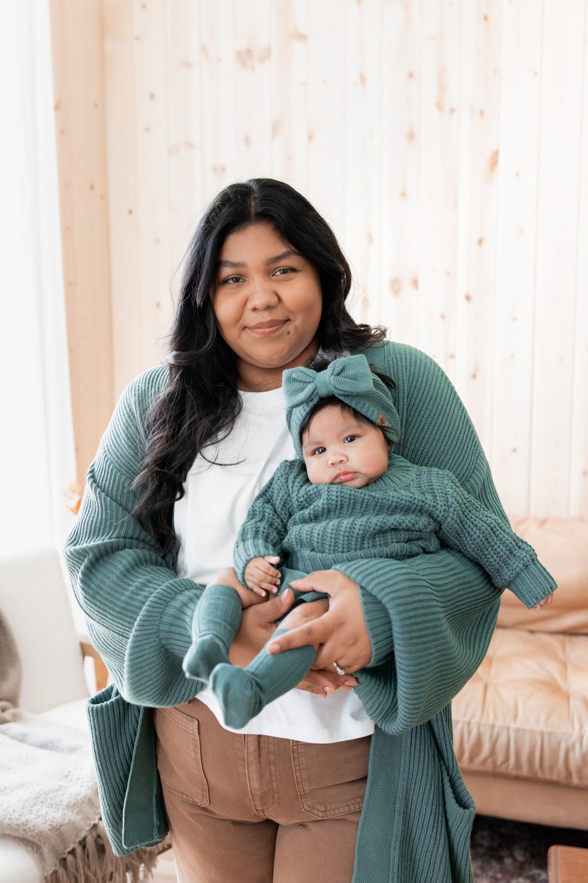 Modal wearing Chunky Knit Women's Oversized Cardigan in Pine holding baby wearing Chunky knit sweater, chunky knit bow headband and socks in pine