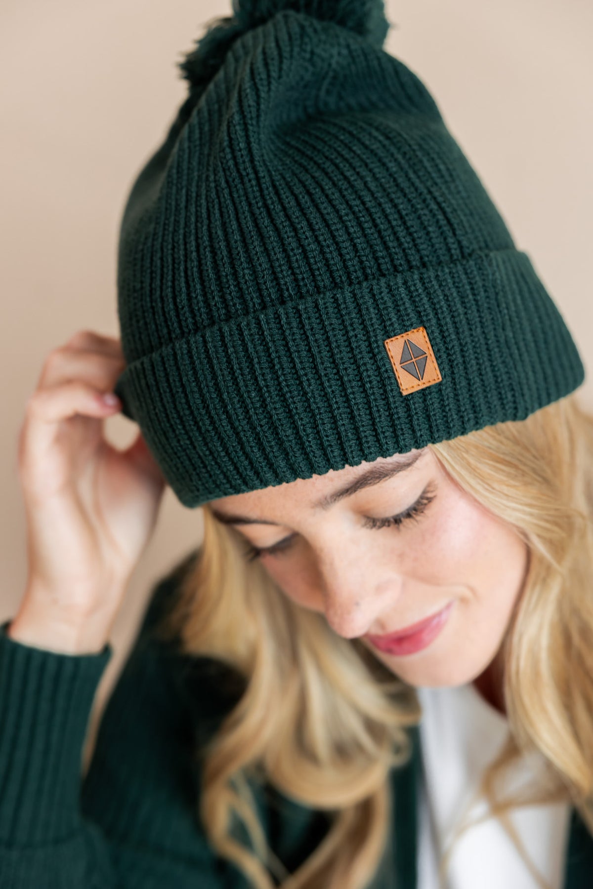 Modal wearing chunky knit adult ribbed beanie in cypress on a beige background
