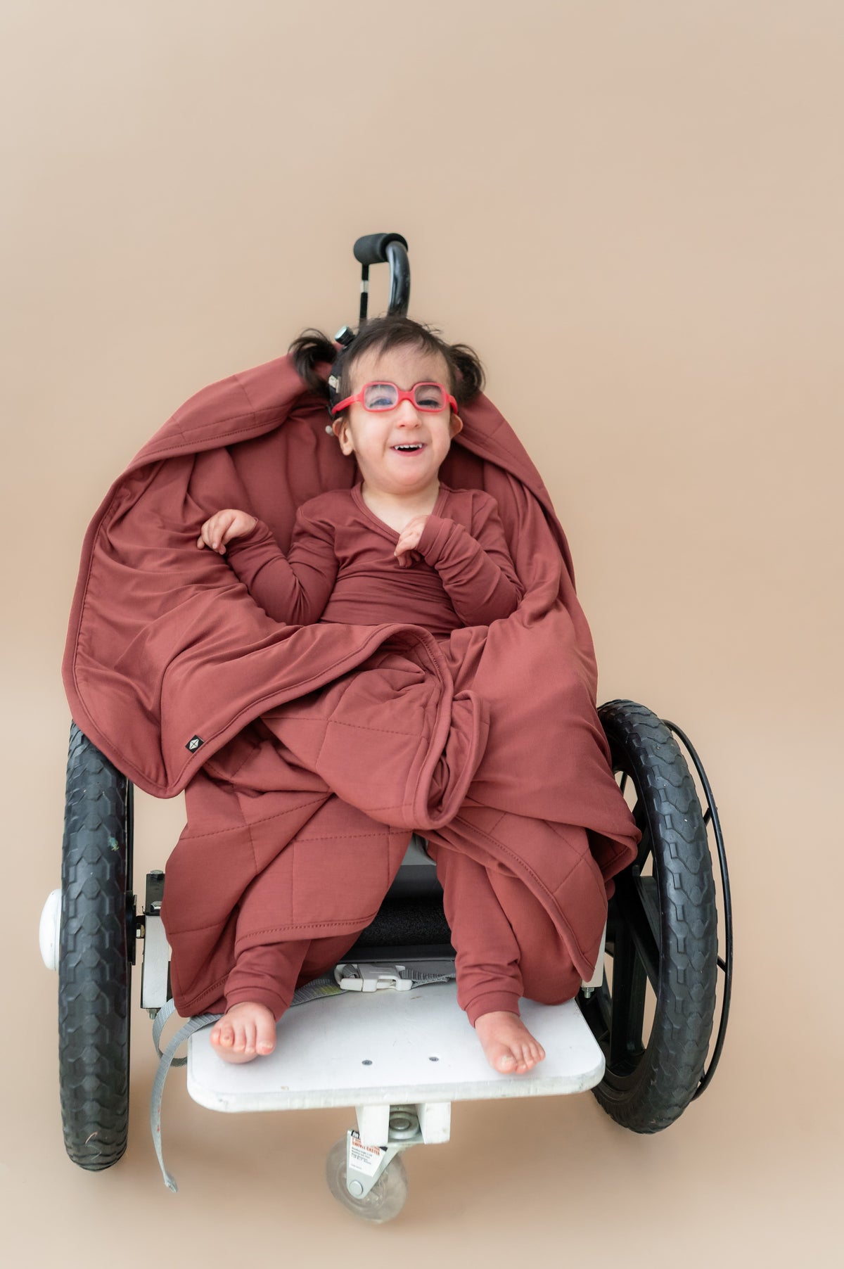 Child sitting on a wheel chair wrapped in Toddler Blanket in Ember 2.5 wearing a similar color long sleeve pajamas