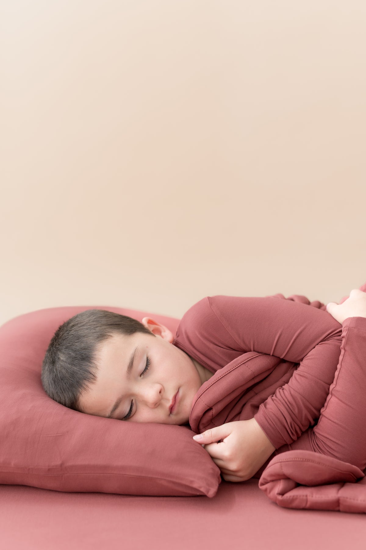 Boy sleeping on Standard Pillowcase in Ember covered under similar color blanket while wearing a similar color shirt