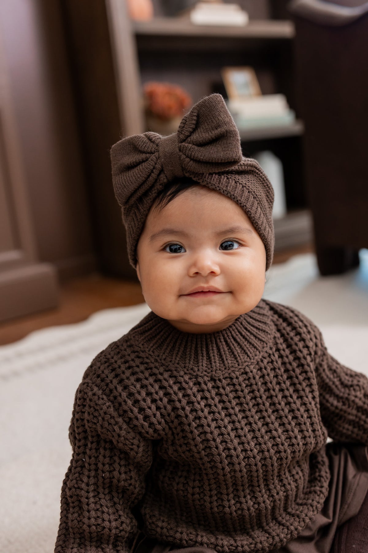 Baby wearing Chunky Knit Bow Headband in Espresso over chunky knit sweater in espresso