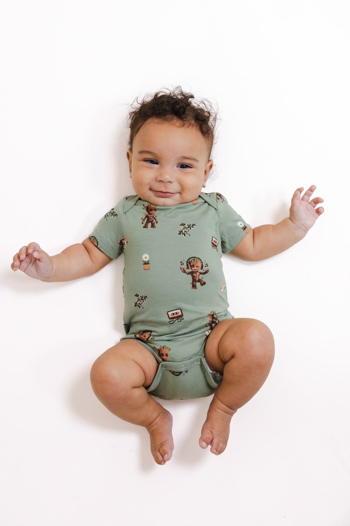 Baby wearing Green Bodysuit in Groot print lying on a white background