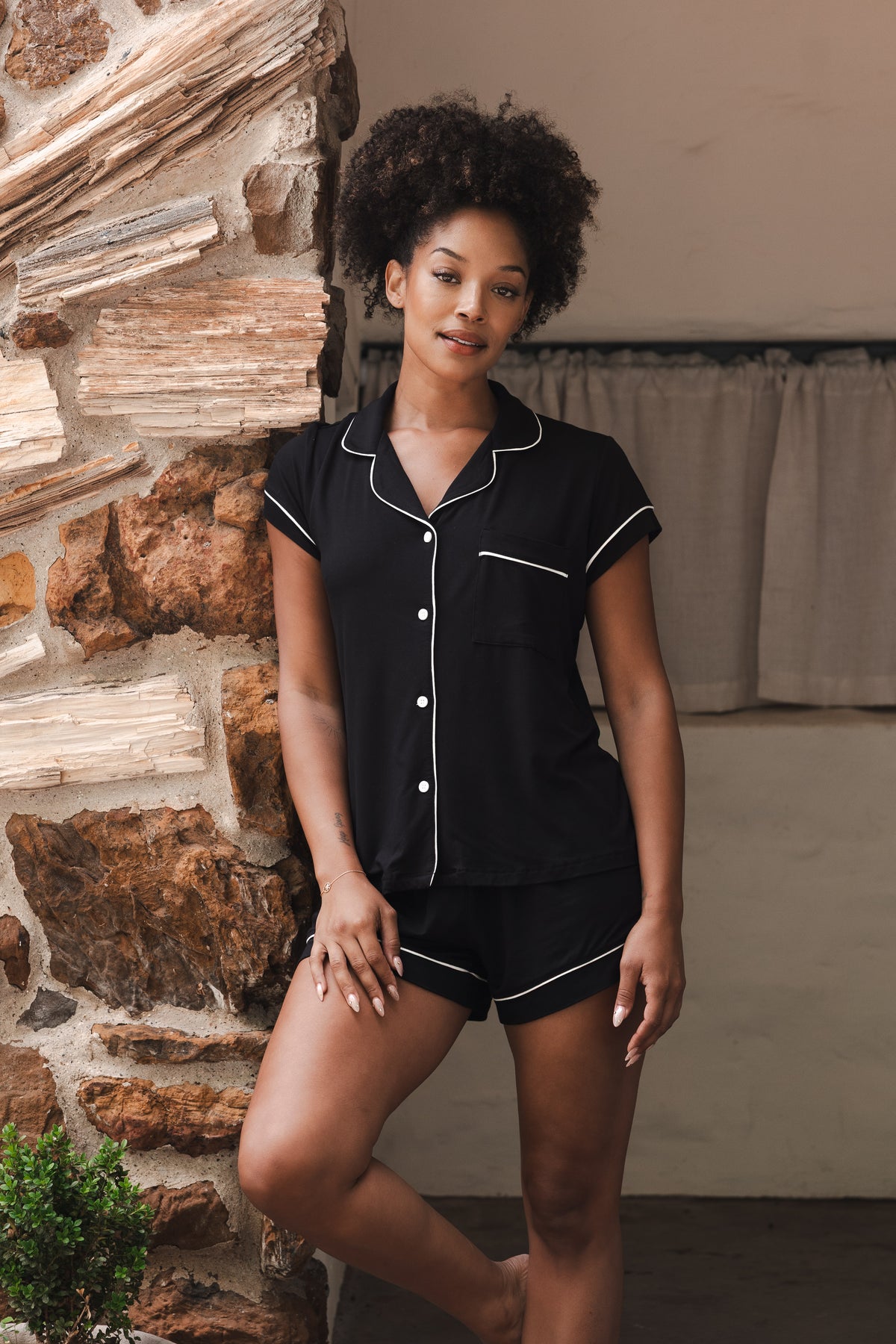 Female model leaning against a rock wall wearing the Women’s Short Sleeve Pajama Set in Midnight with Cloud Trim