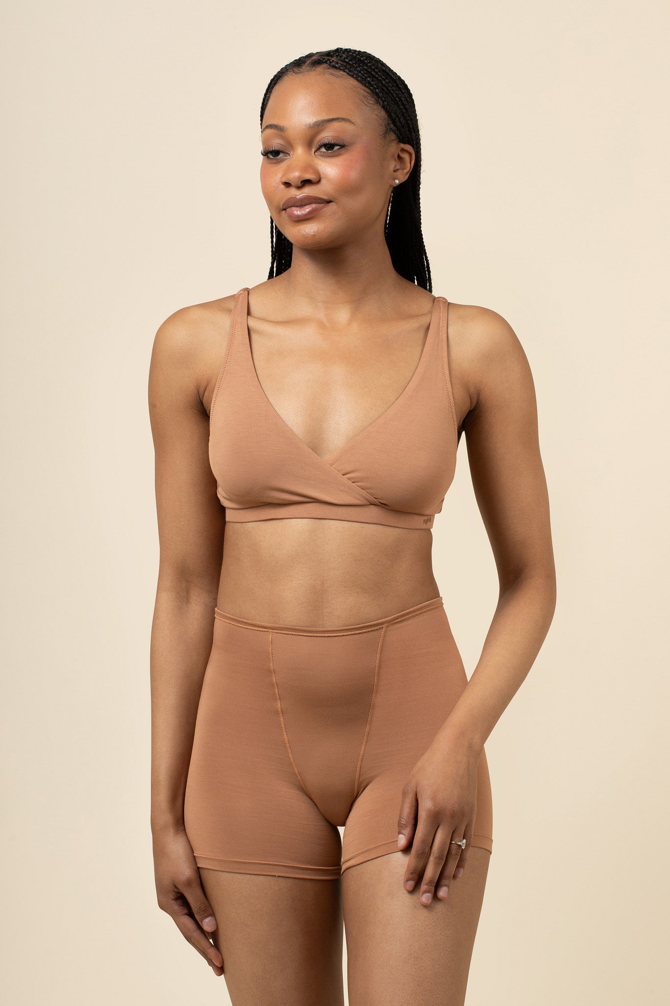 Woman wearing a brown boxer and bra against a beige background