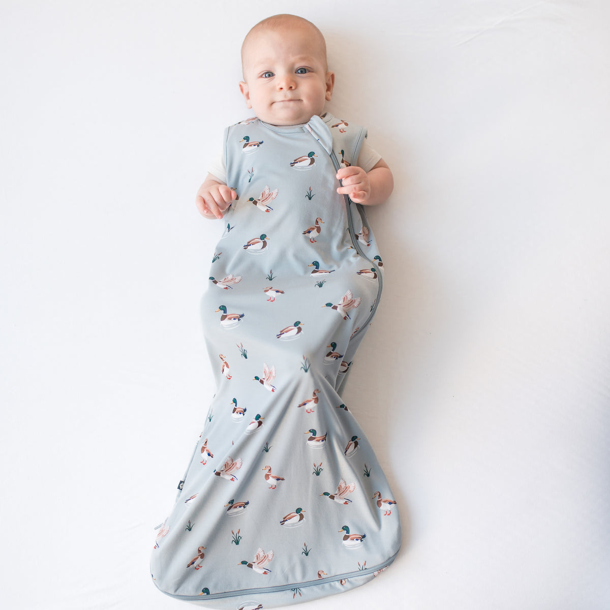 Infant laying on a white surface wearing the Sleep Bag in Mallard