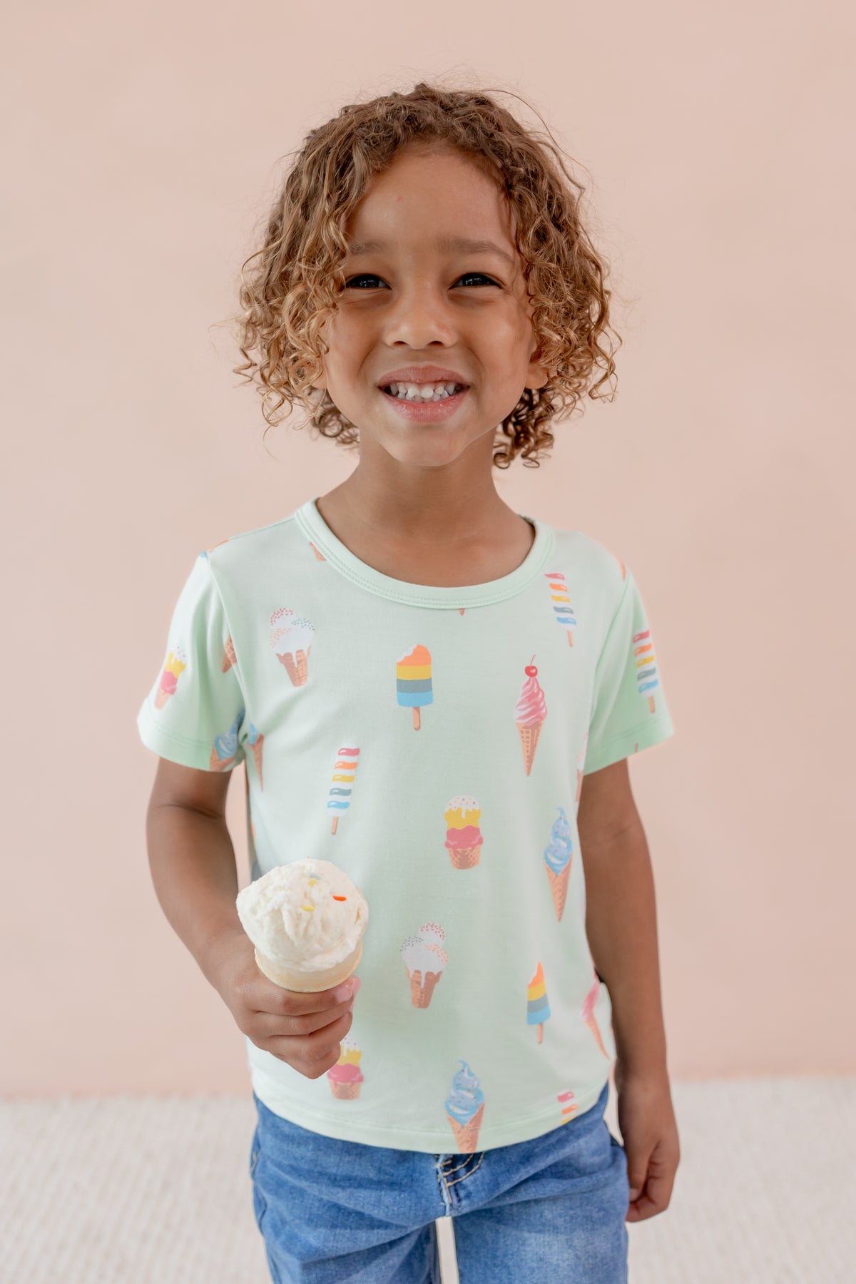 Child smiling holding an ice cream cone wearing Toddler Basic Tee in Mint Ice Cream over Denim pants print on a beige background