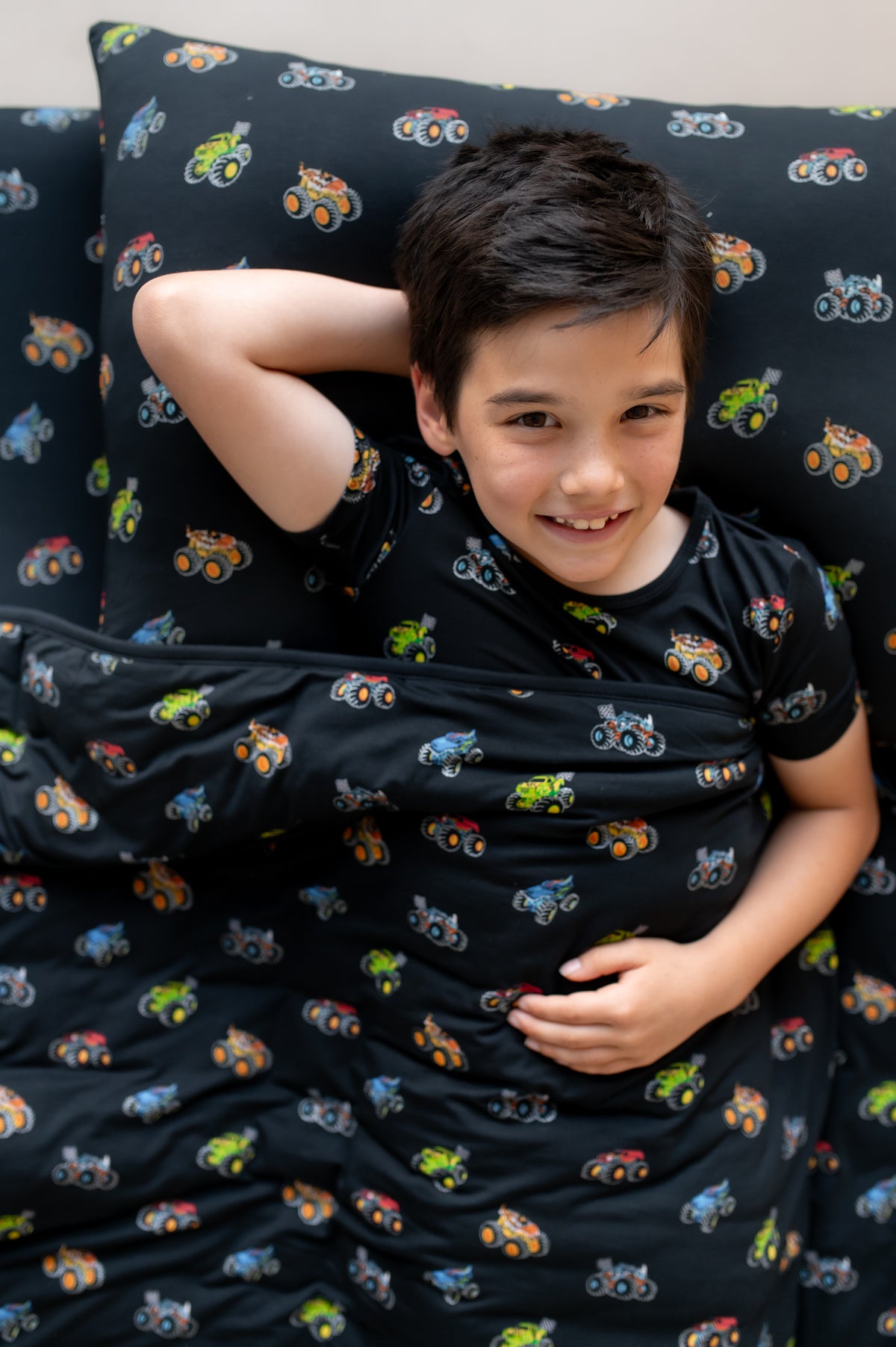 Boy lying on black Standard Pillowcase and sheet in Monster Truck print covered with similar print Blanket