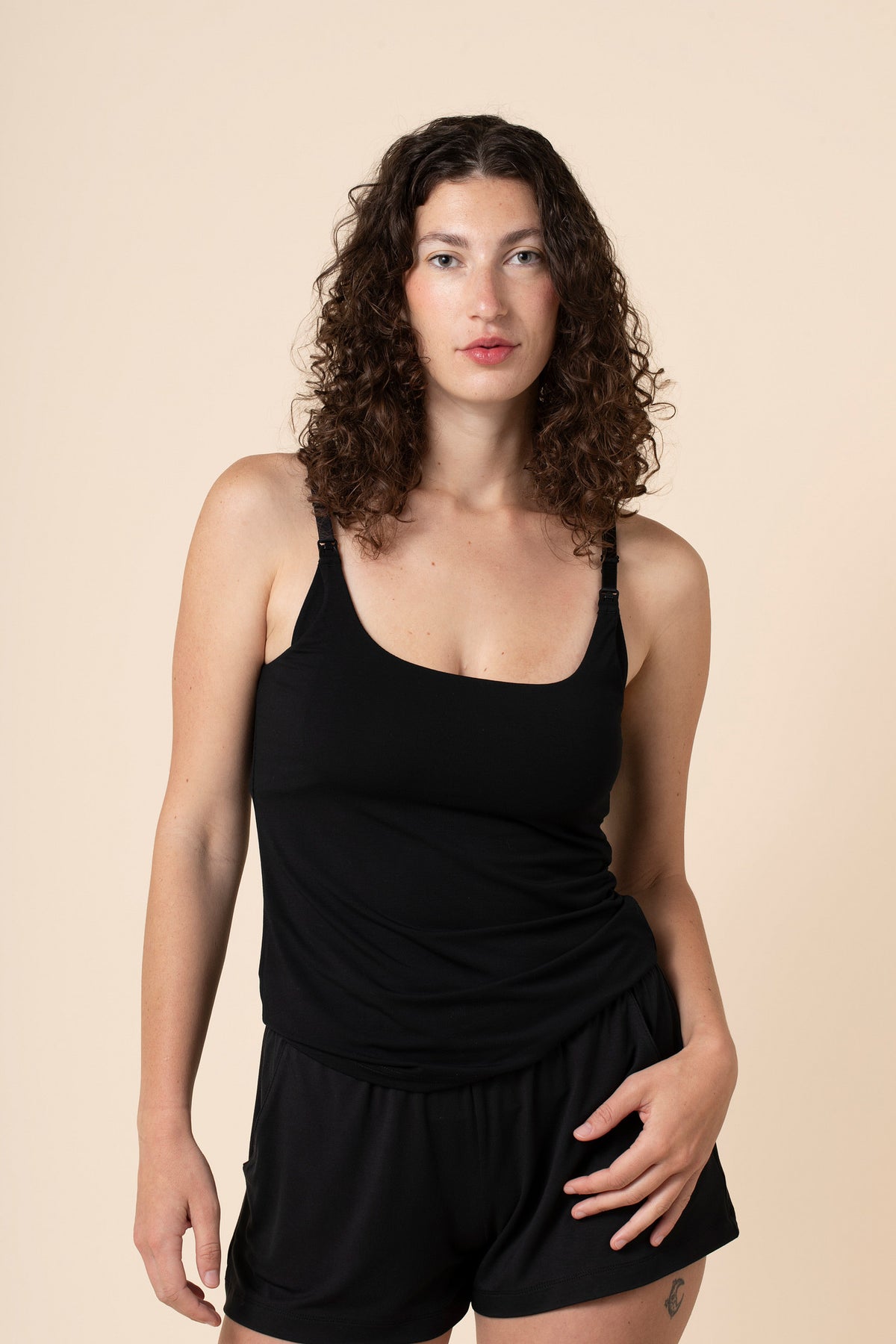 Woman wearing a black sleeveless nursing top and shorts on a beige background