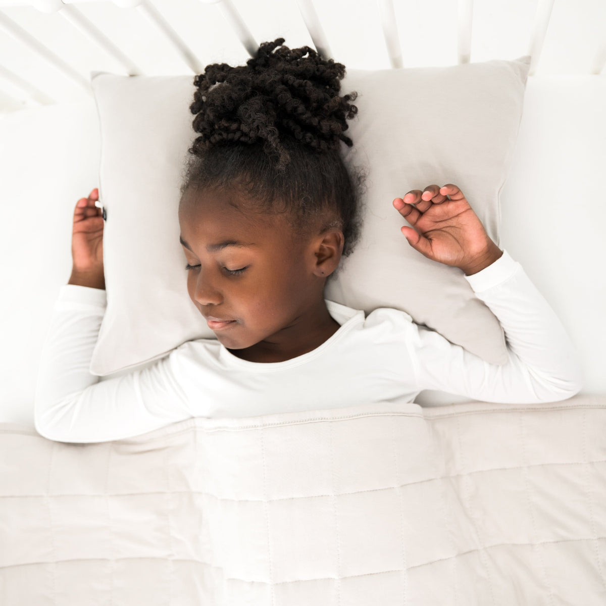 Young girl lying on a bed with white bedding and cream pillow.