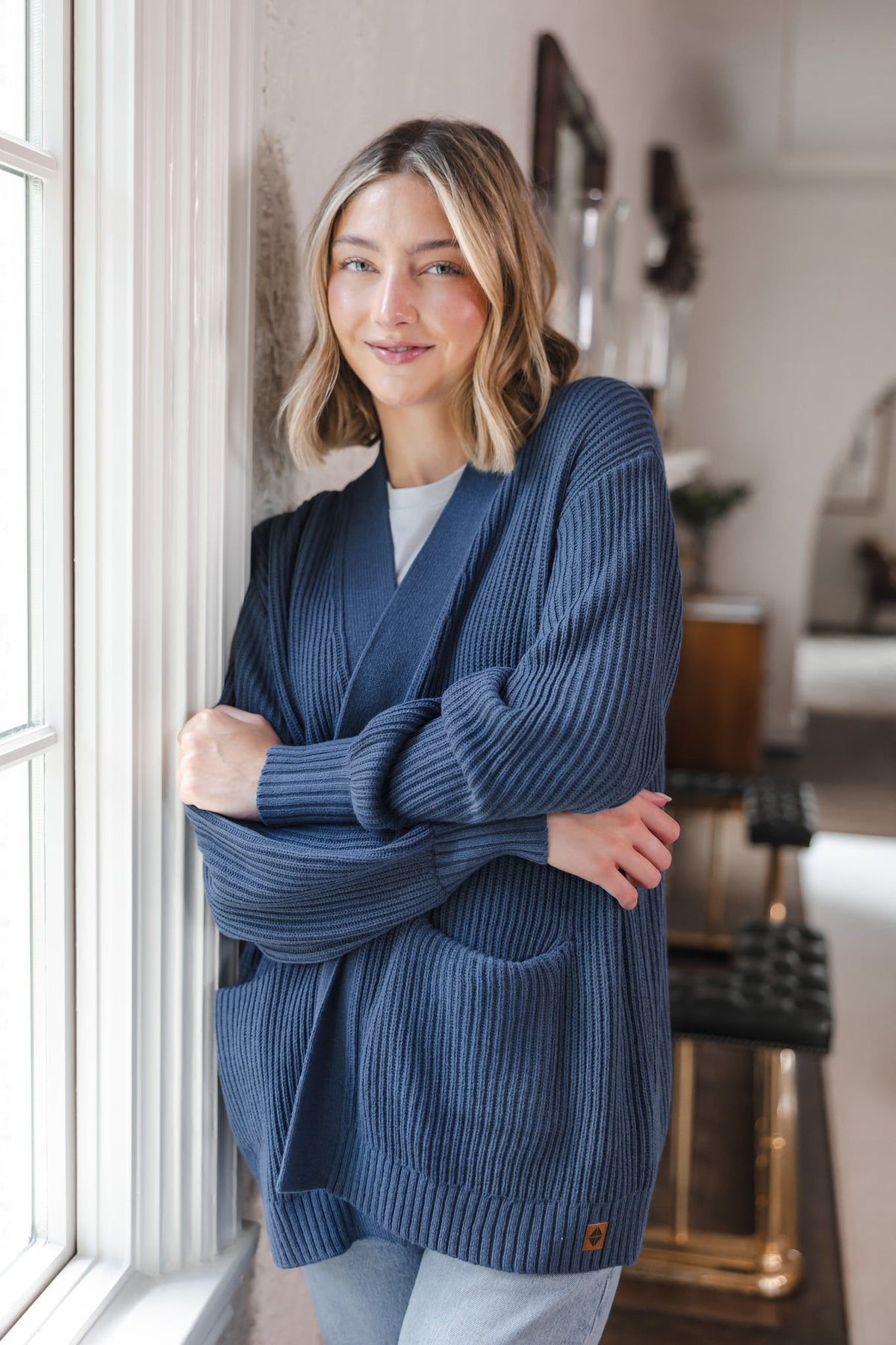 Modal standing against a wall wearing chunky knit oversized cardigan in oxford over blue jeans and white t-shirt
