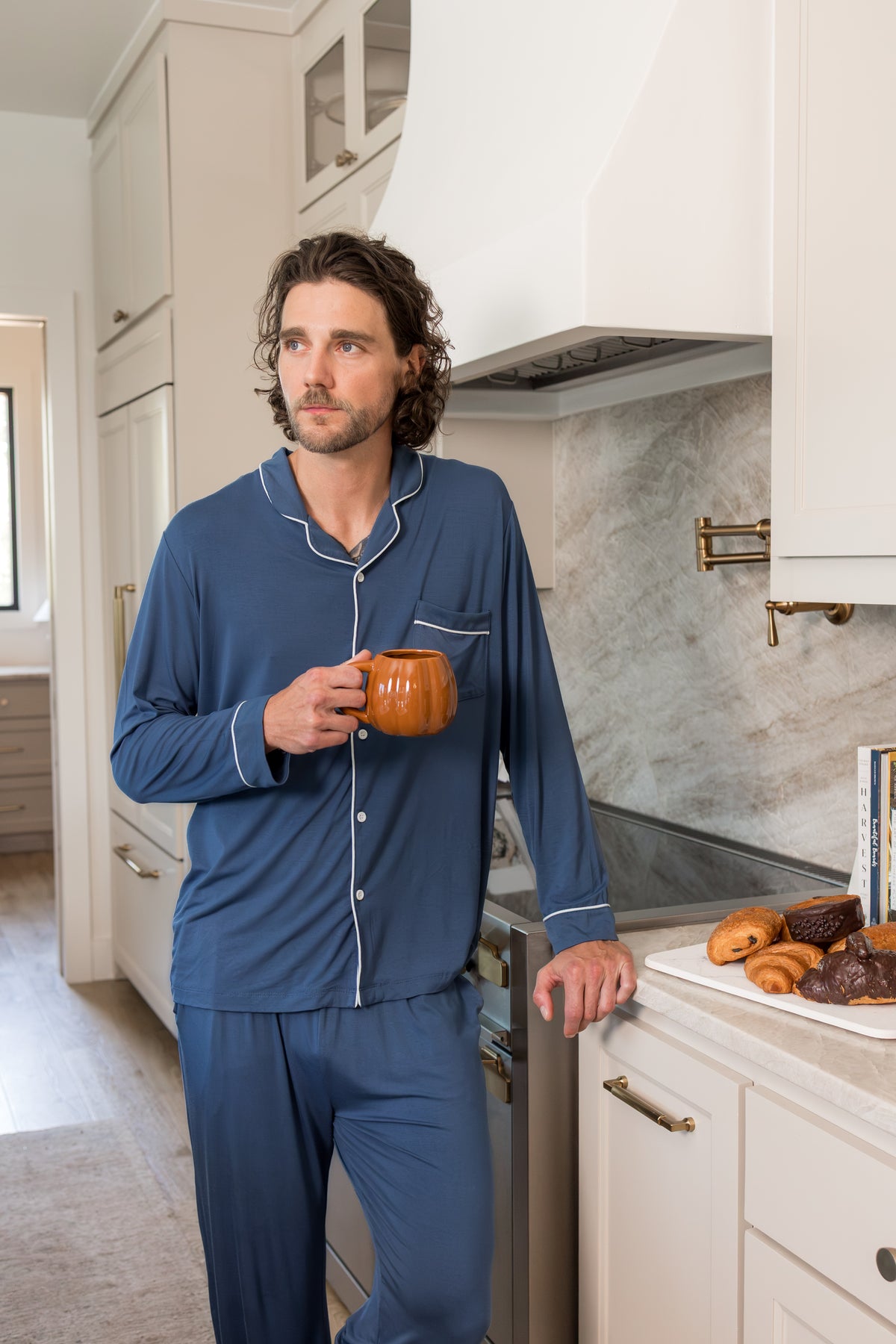 Model wearing Men's Long Sleeve Pajama Set in Oxford standing in a kitchen with a mug