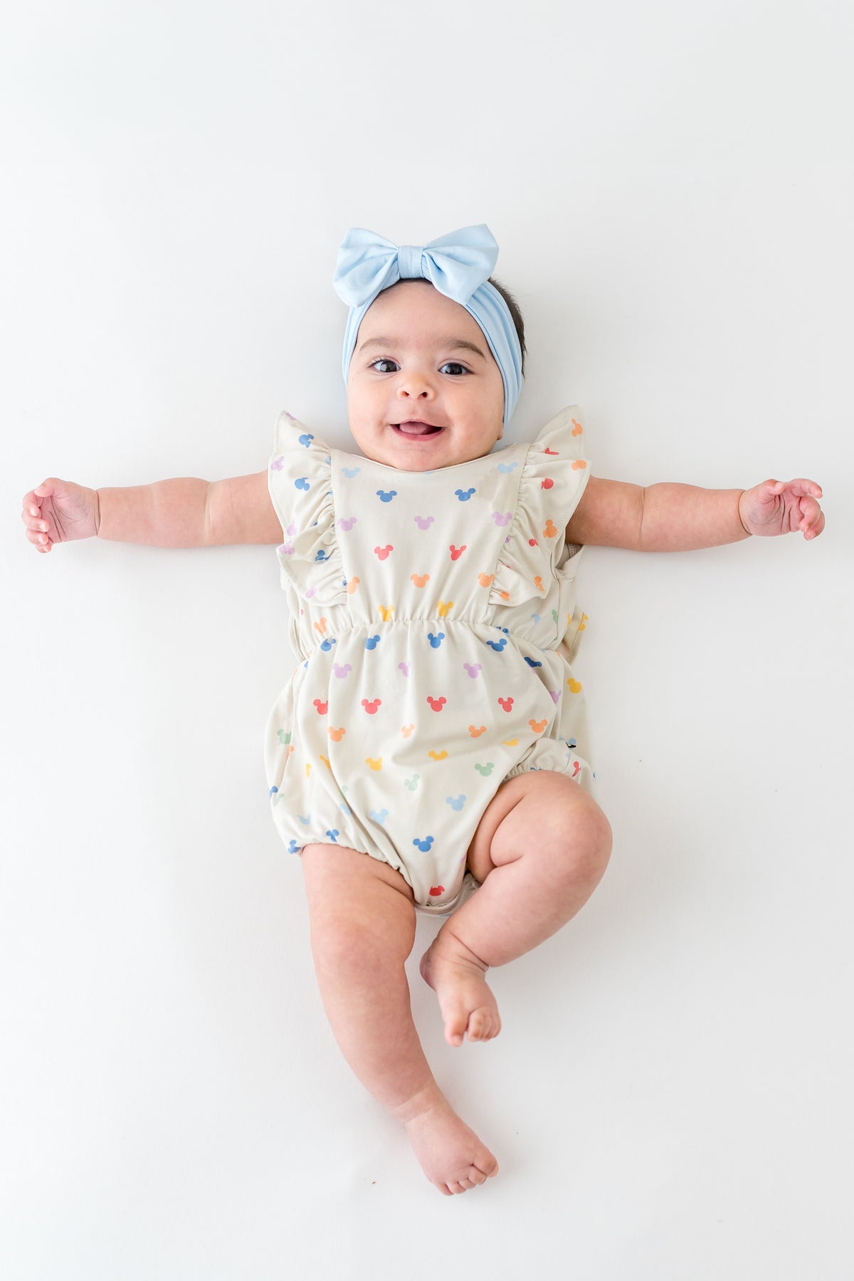 Baby in a pastel Mickey Mouse head printed bubble romper and blue bow
