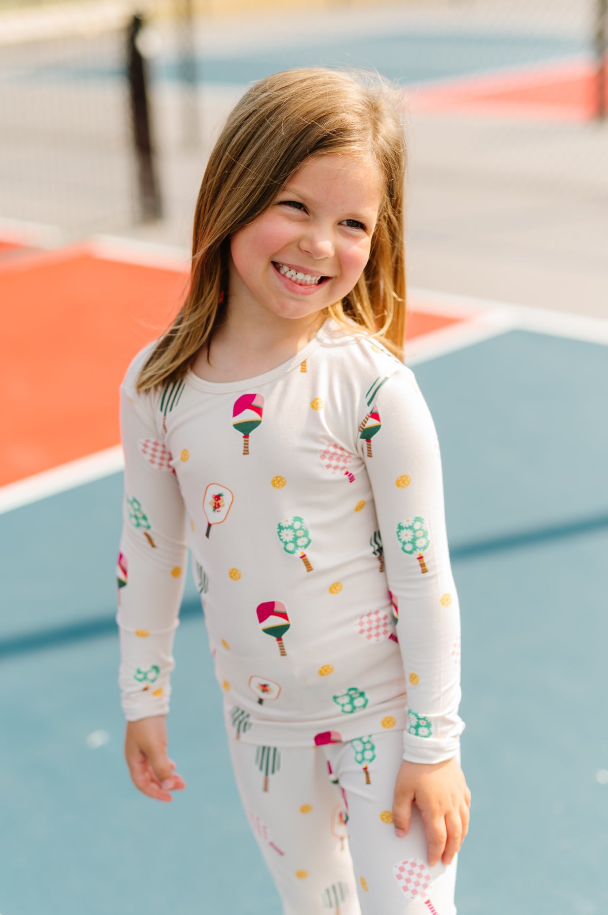 Girl smiling in Long Sleeve Pajamas in Pickleball print standing on pickleball court