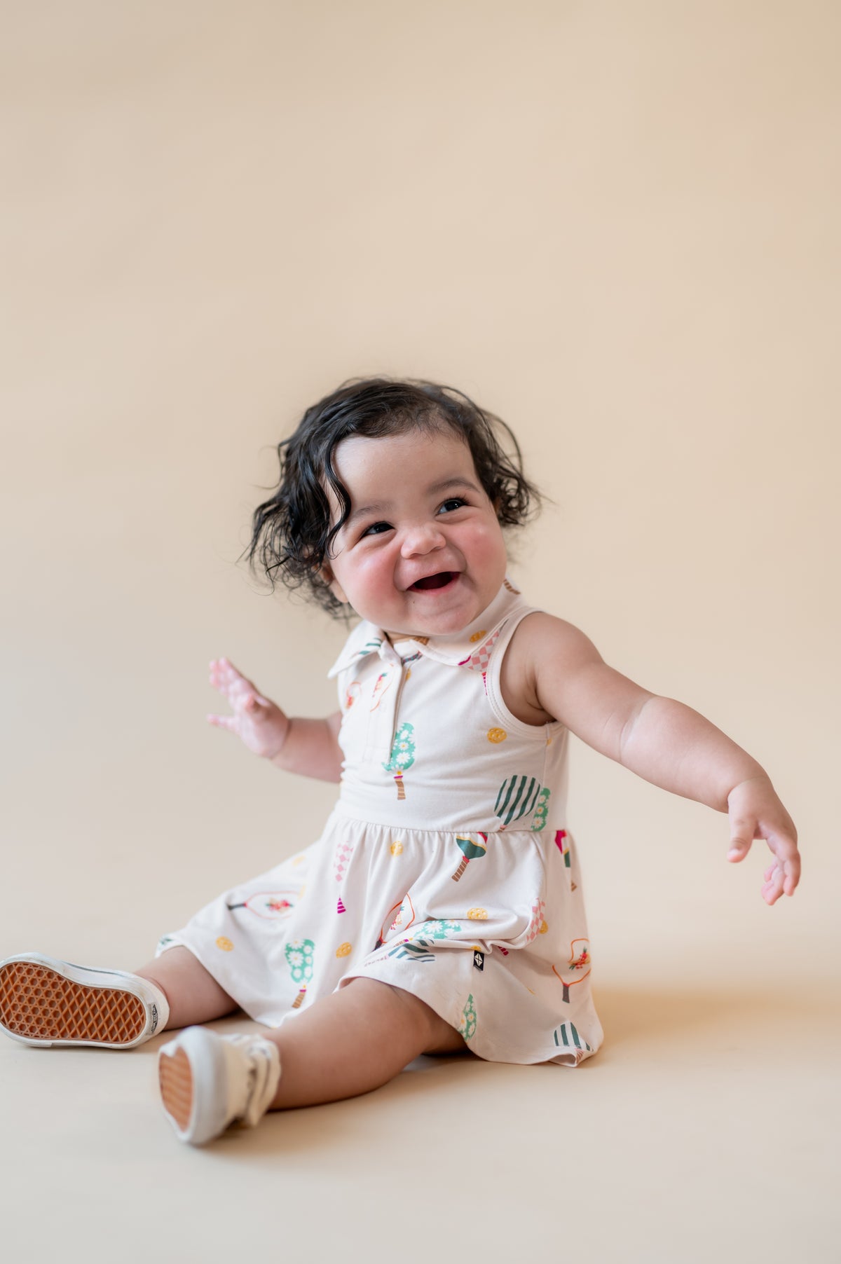 Baby posing in Polo Bodysuit Dress with Pickleball print on a beige background