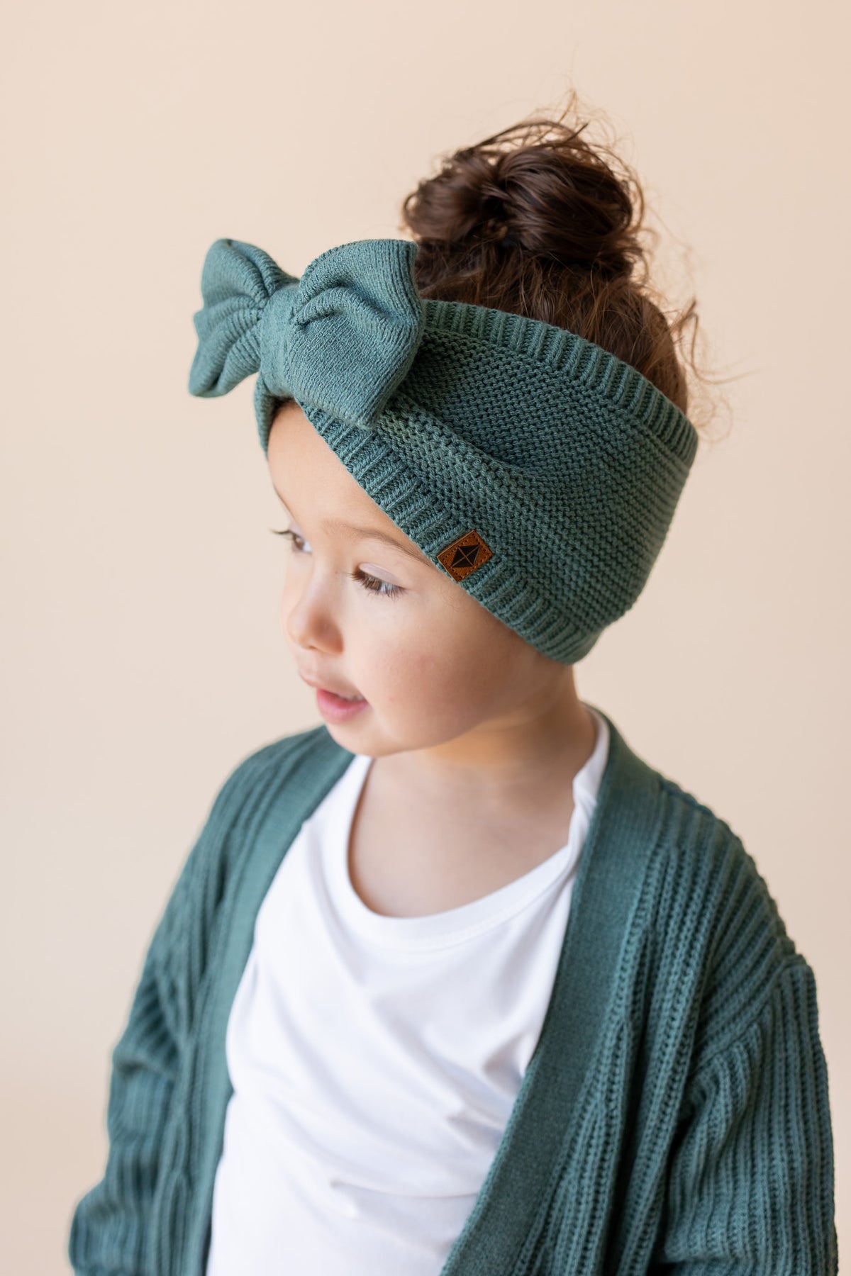 Modal wearing Chunky Knit Bow Headband in Pine over white T-shirt and Chunky knit oversized cardigan in pine on a beige background