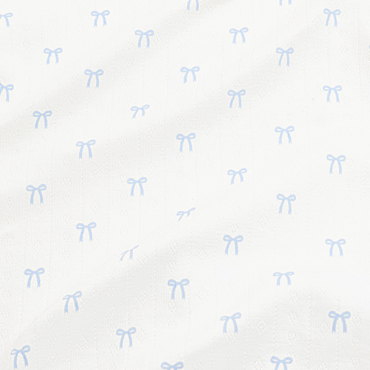 Close up of the pointelle fabric: An all-over print of dainty light blue bows over a white background.
