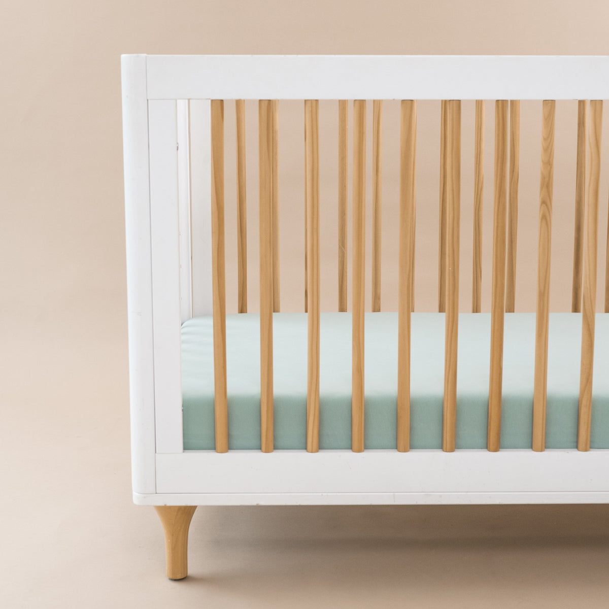 Crib Sheet in Sage shown on a mattress in a modern white and wooden crib