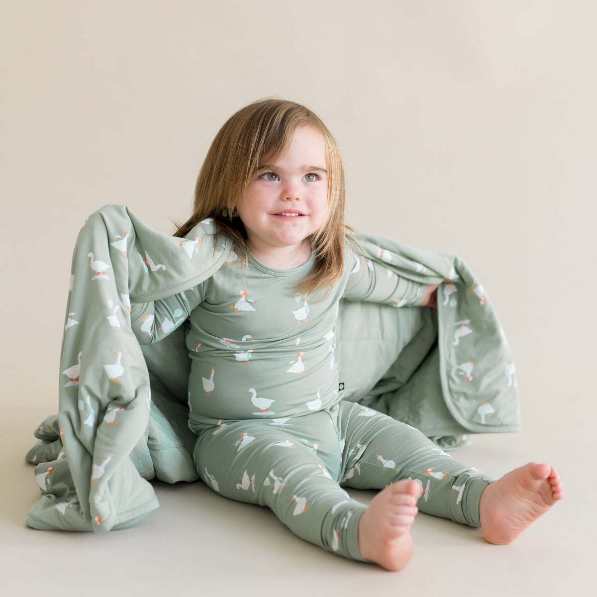 child in a silly goose printed pajama set and matching blanket wrapped around them