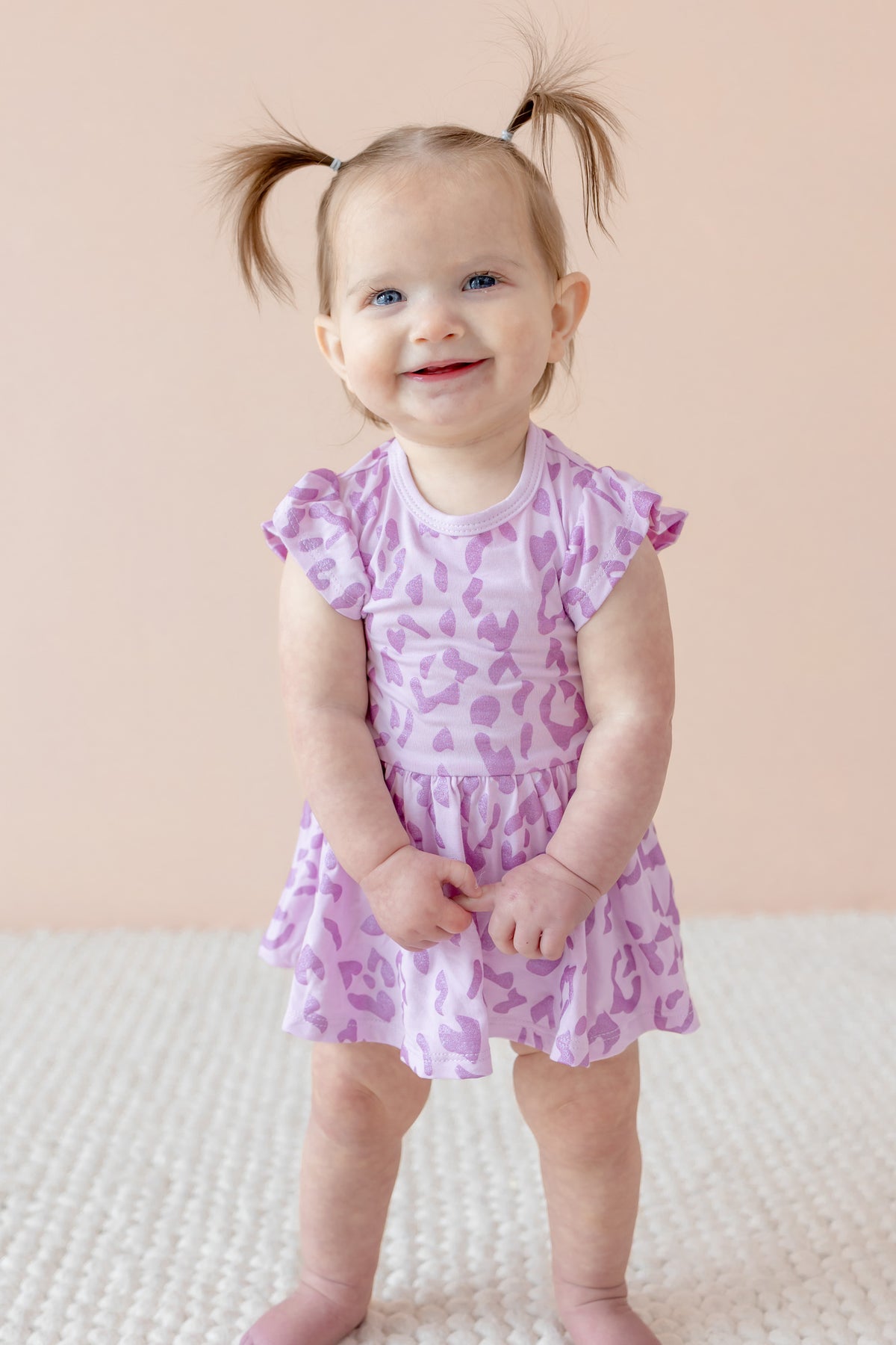 Child wearing Twirl bodysuit dress in Thistle Leopard print on a beige background