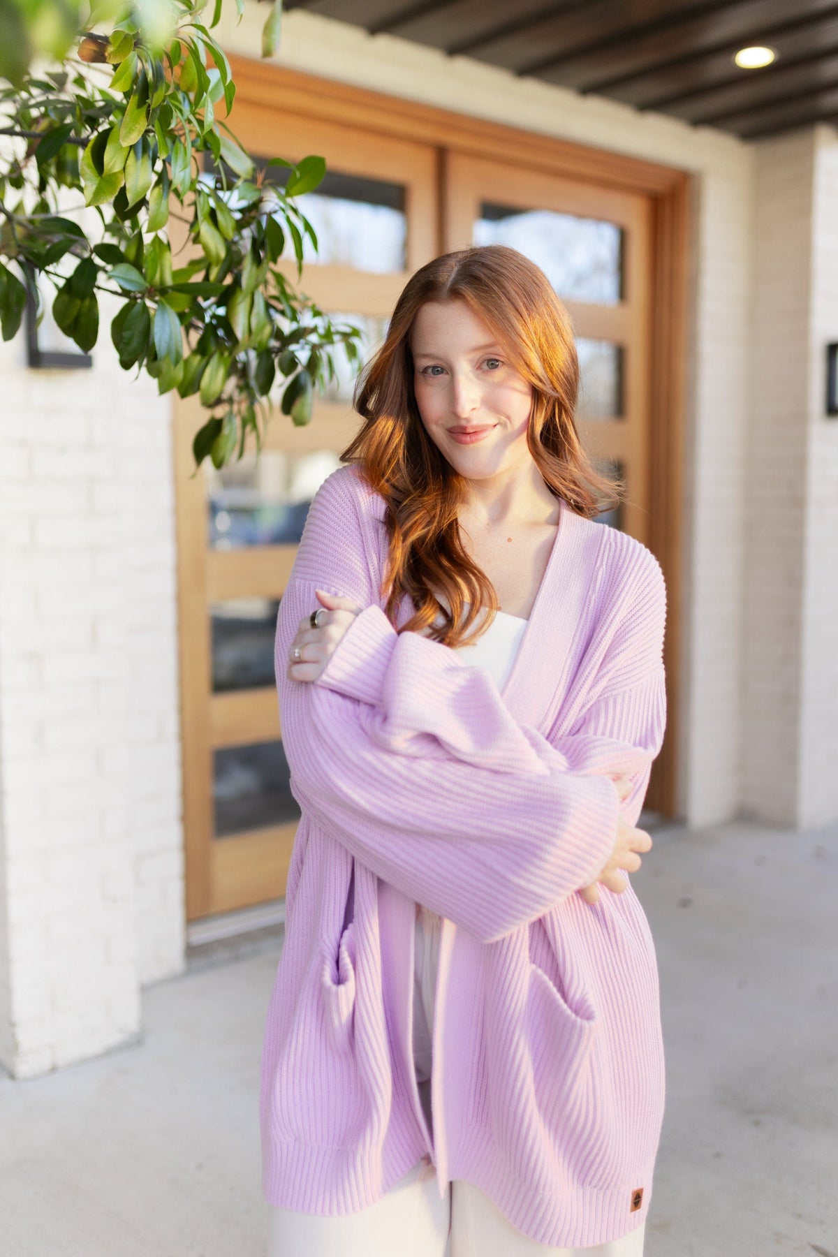 Woman wearing a light purple cardigan standing in front of a wooden door.