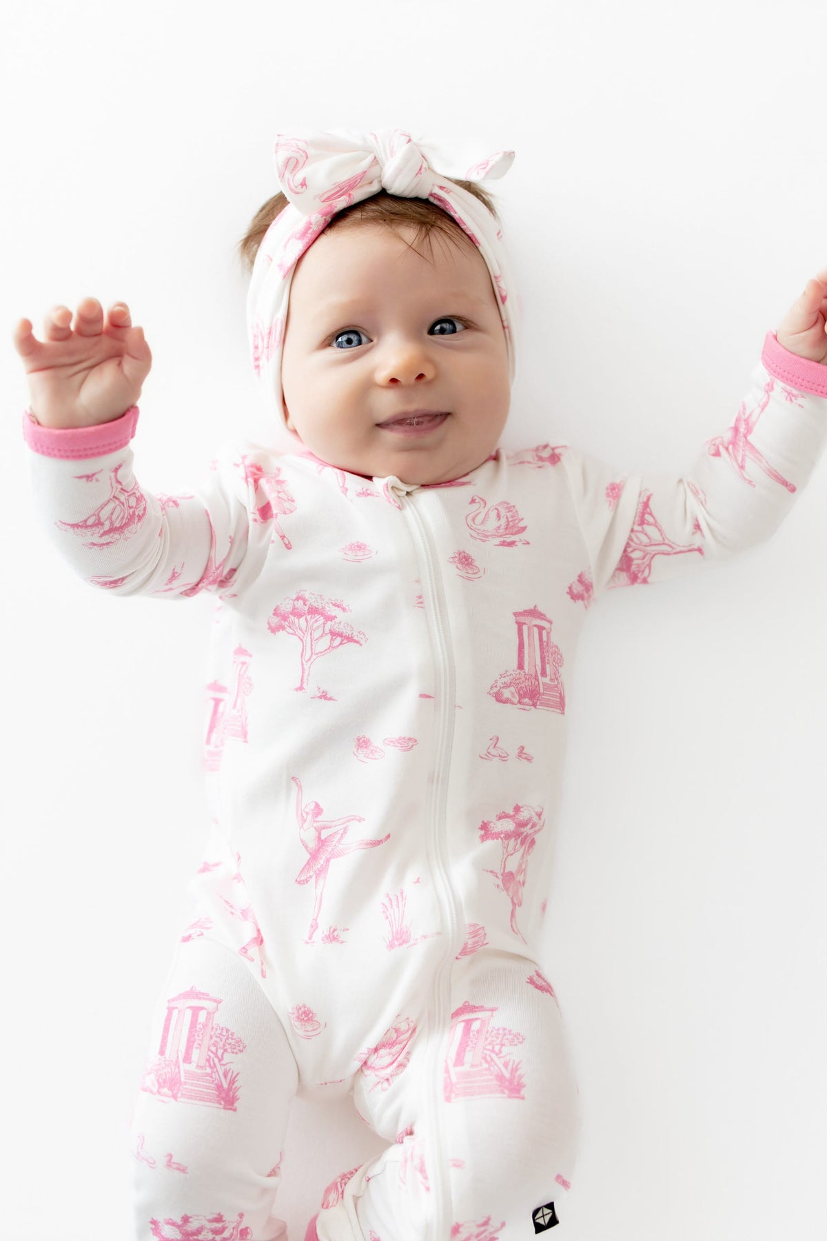 Close up of infant wearing the Zippered Romper in Toile Ballet and matching bow