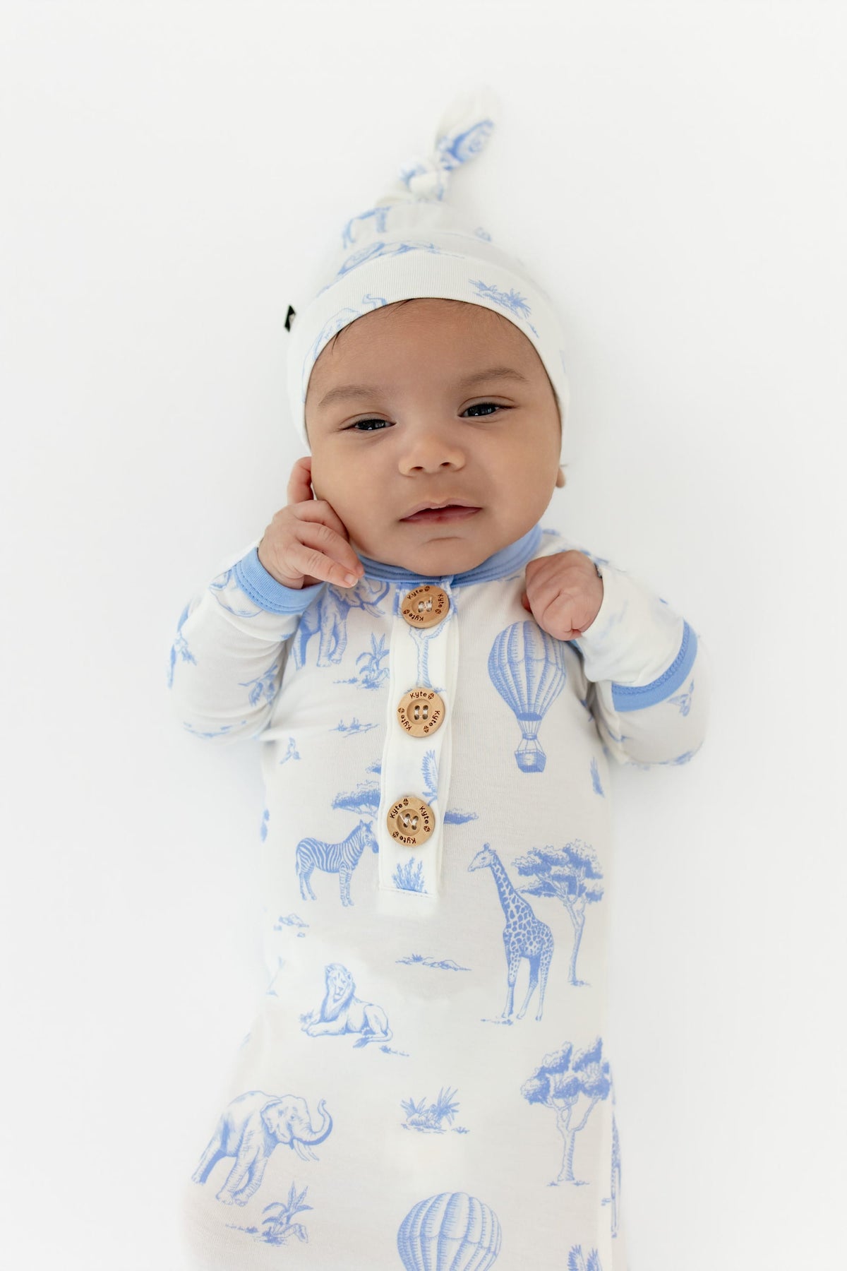 Close up of infant wearing the Knotted Gown with Hat Set in Toile Safari showing the Kyte Baby engraved wooden buttons