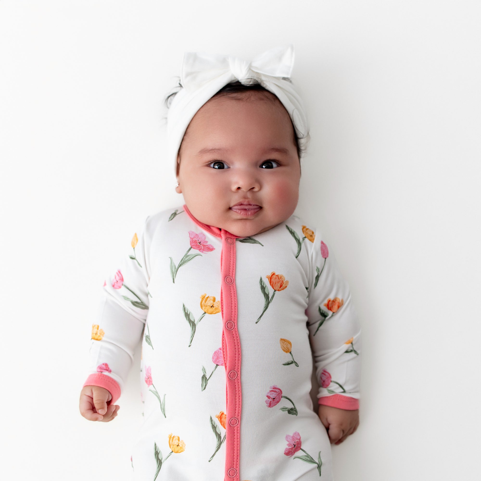 Close up of a newborn wearing the Romper in Tulip and white bow headband