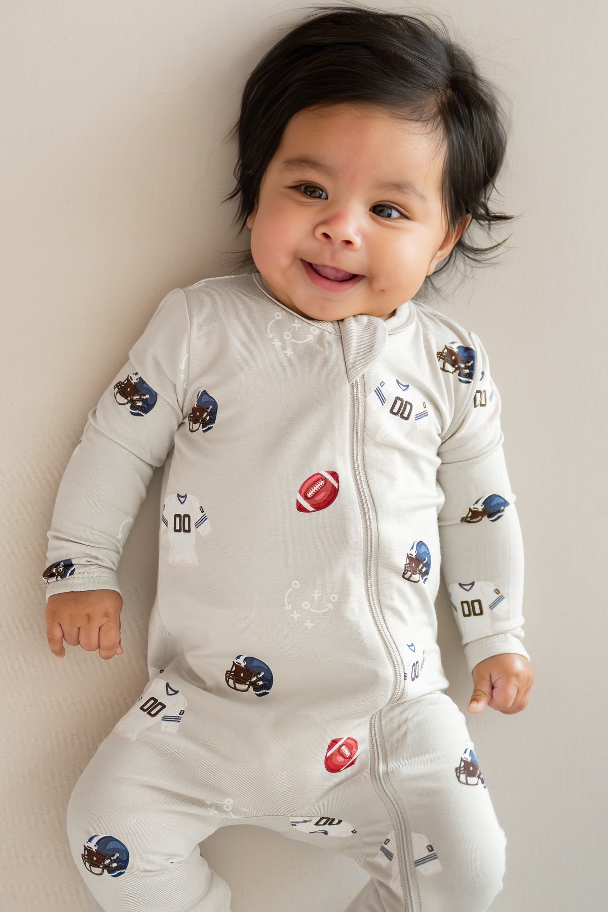 Baby wearing Zippered Footie in Vintage Football print on a beige background