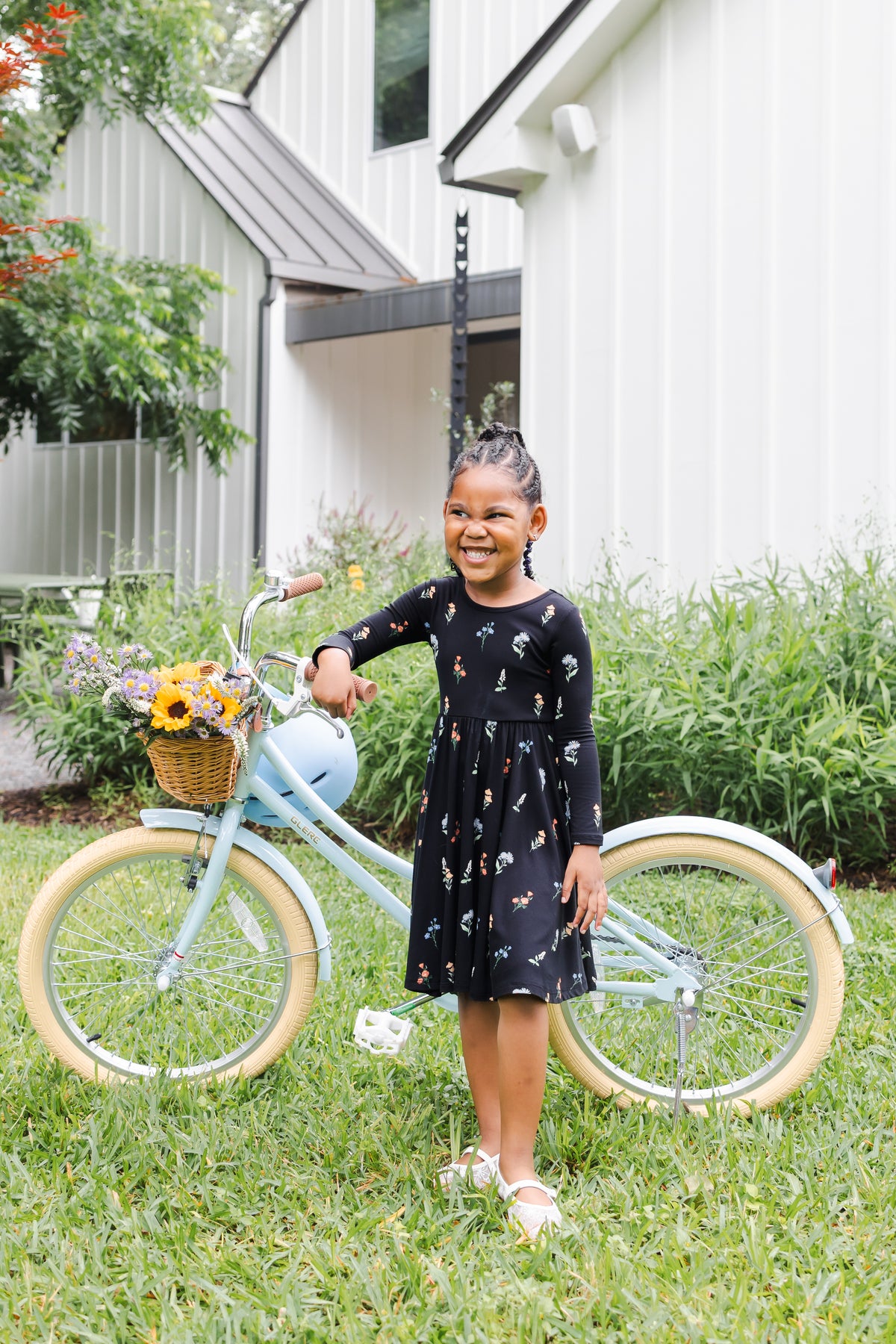 Girl standing outdoors with a bicycle in a garden wearing Long Sleeve Twirl Dress in Midnight Wildflower print