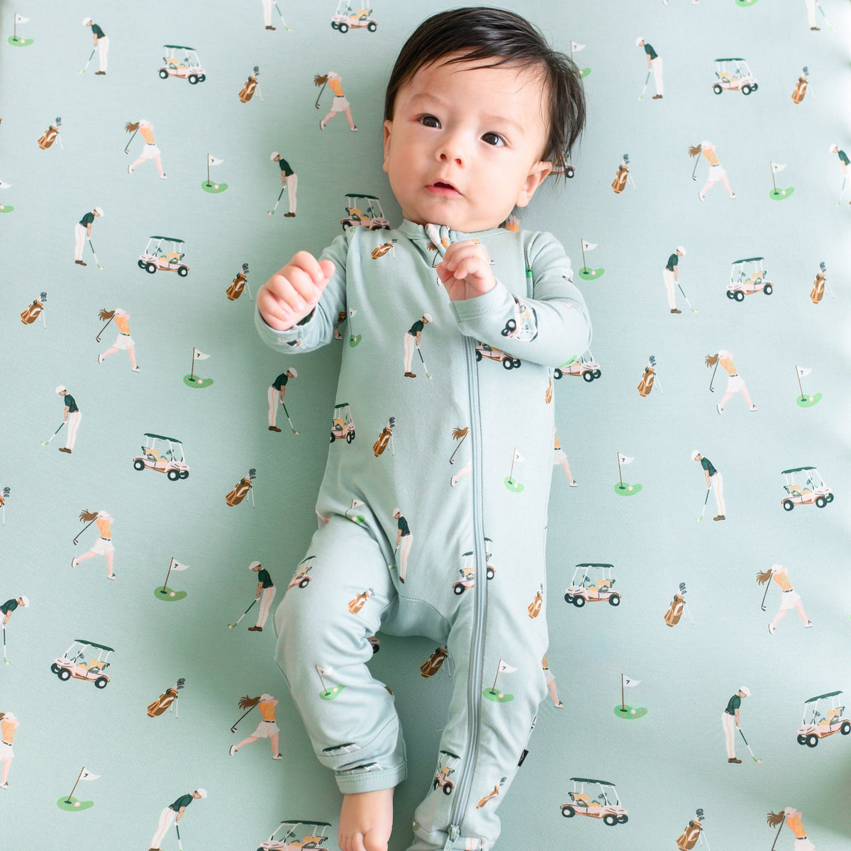 Infant wearing Zippered Romper pajamas laying on Golf Crib Sheet