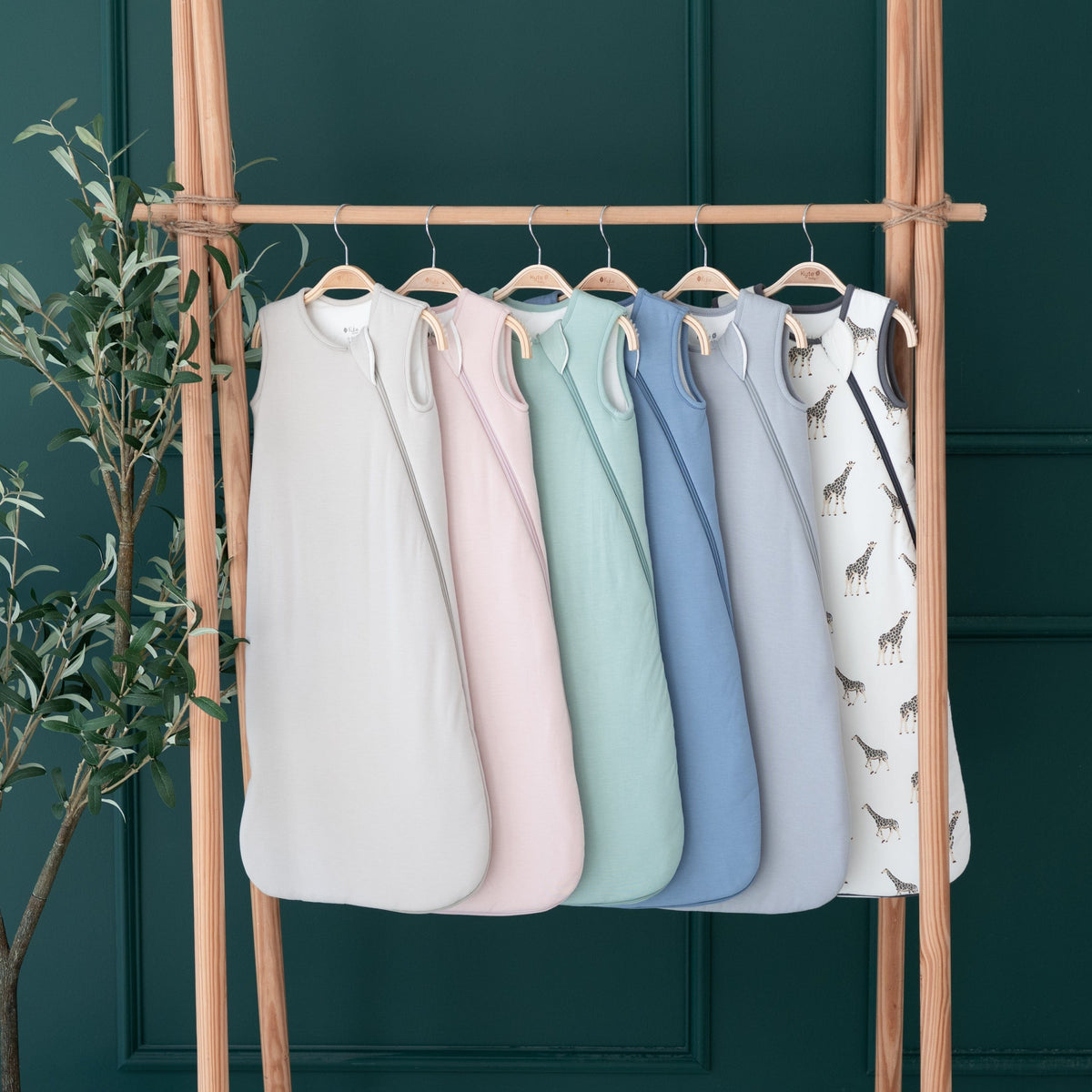 Kyte Baby 2.5 TOG Sleep Bags in core colors and giraffe print hung on hangers on a wooden rack