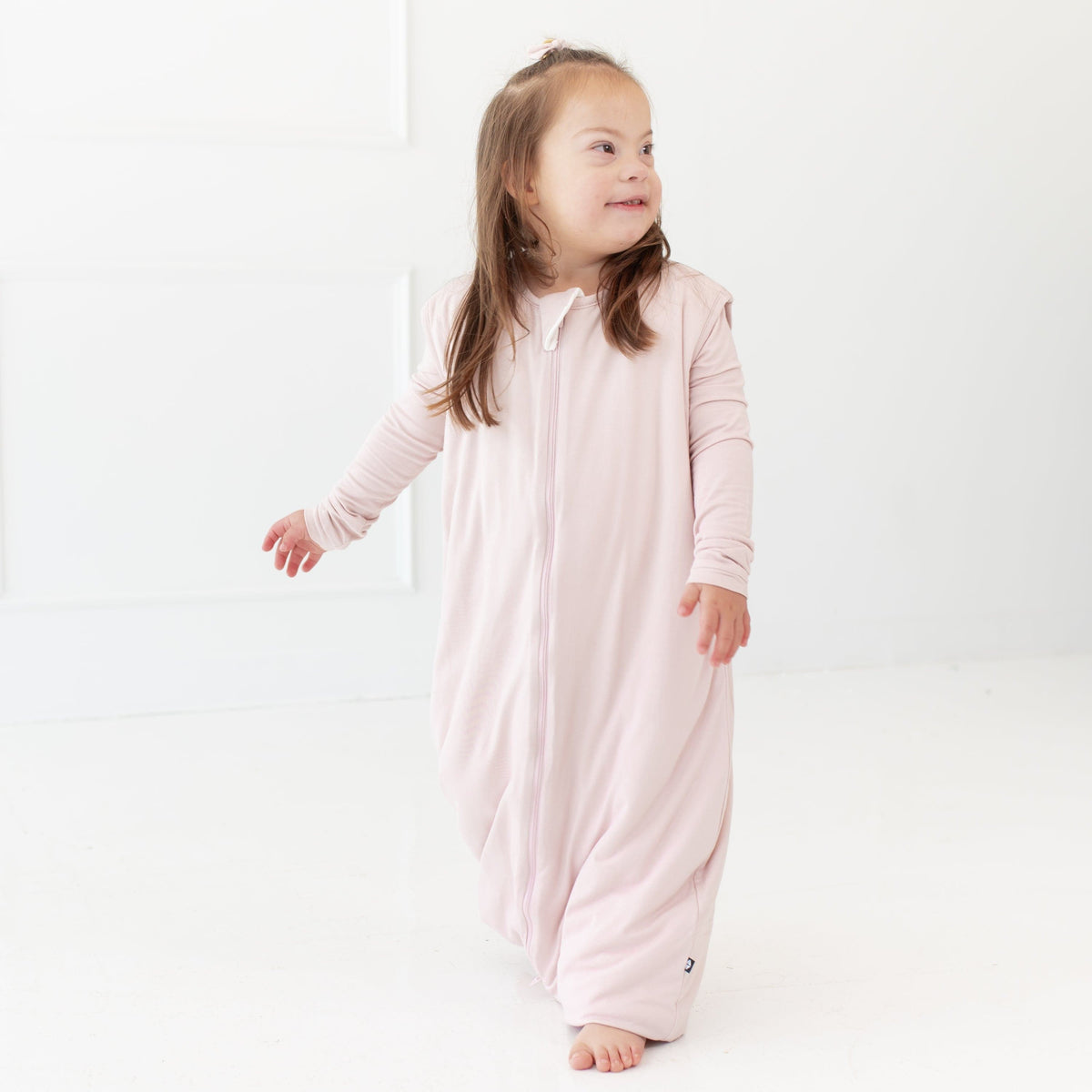 Standing toddler looking to the right hand side while wearing a Kyte Baby Sleep Bag Walker 1.0 in Blush