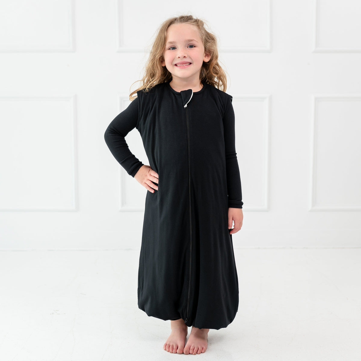 Girl model standing infront of whilte wall while wearing Sleep Bag Walker in Midnight 1.0 with one hand on her waist