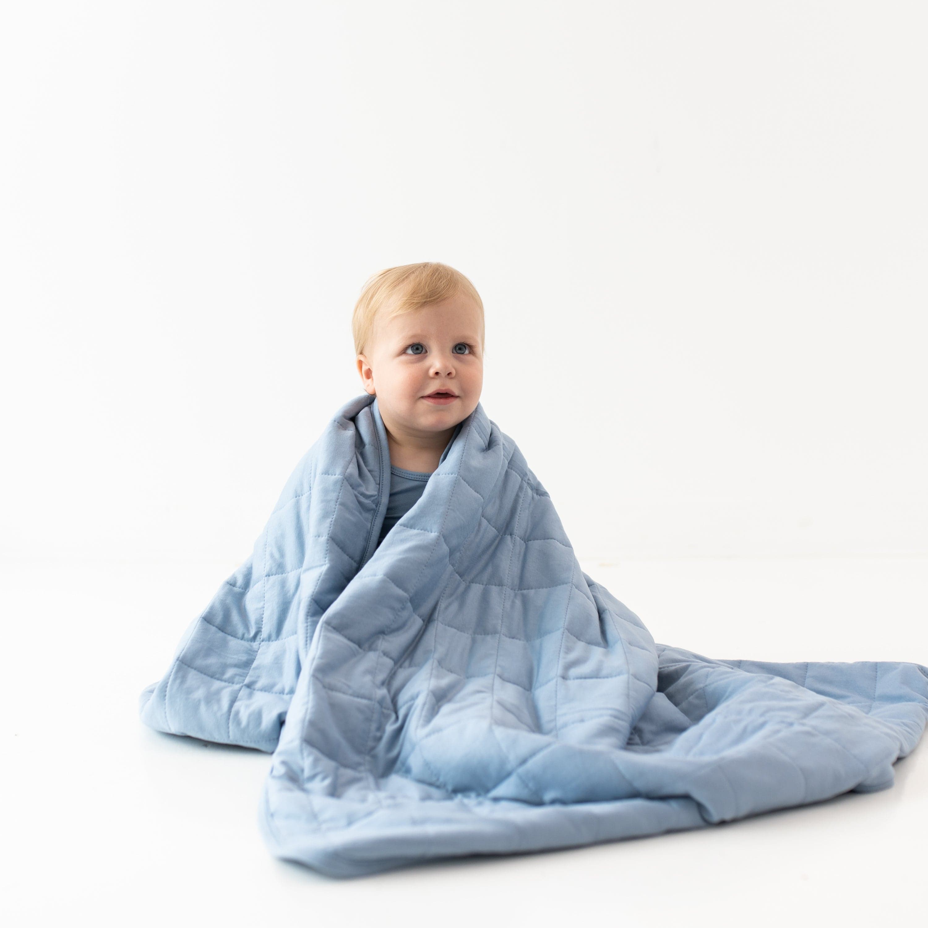 Child sitting in a white room wrapped in a Toddler Blanket in Slate 2.5 TOG